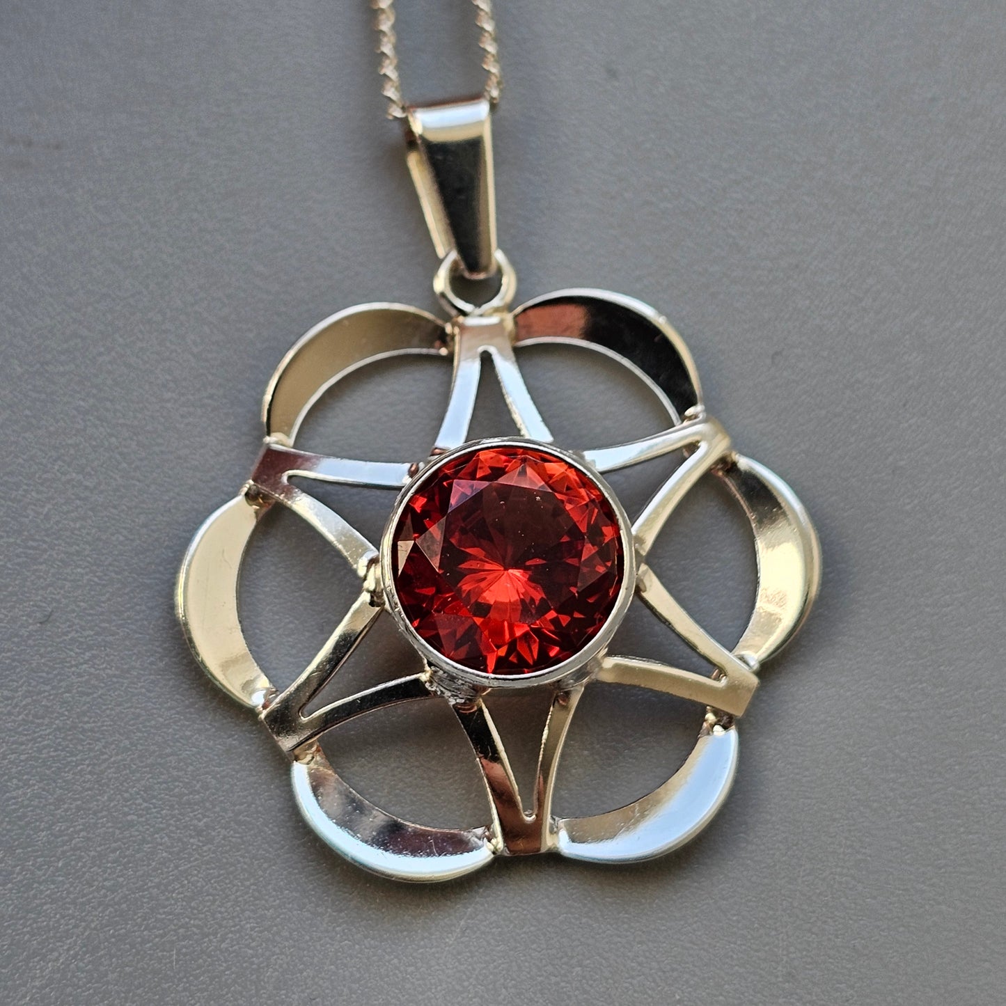 Ornate silver pendant featuring a star-shaped design with a central red gemstone.