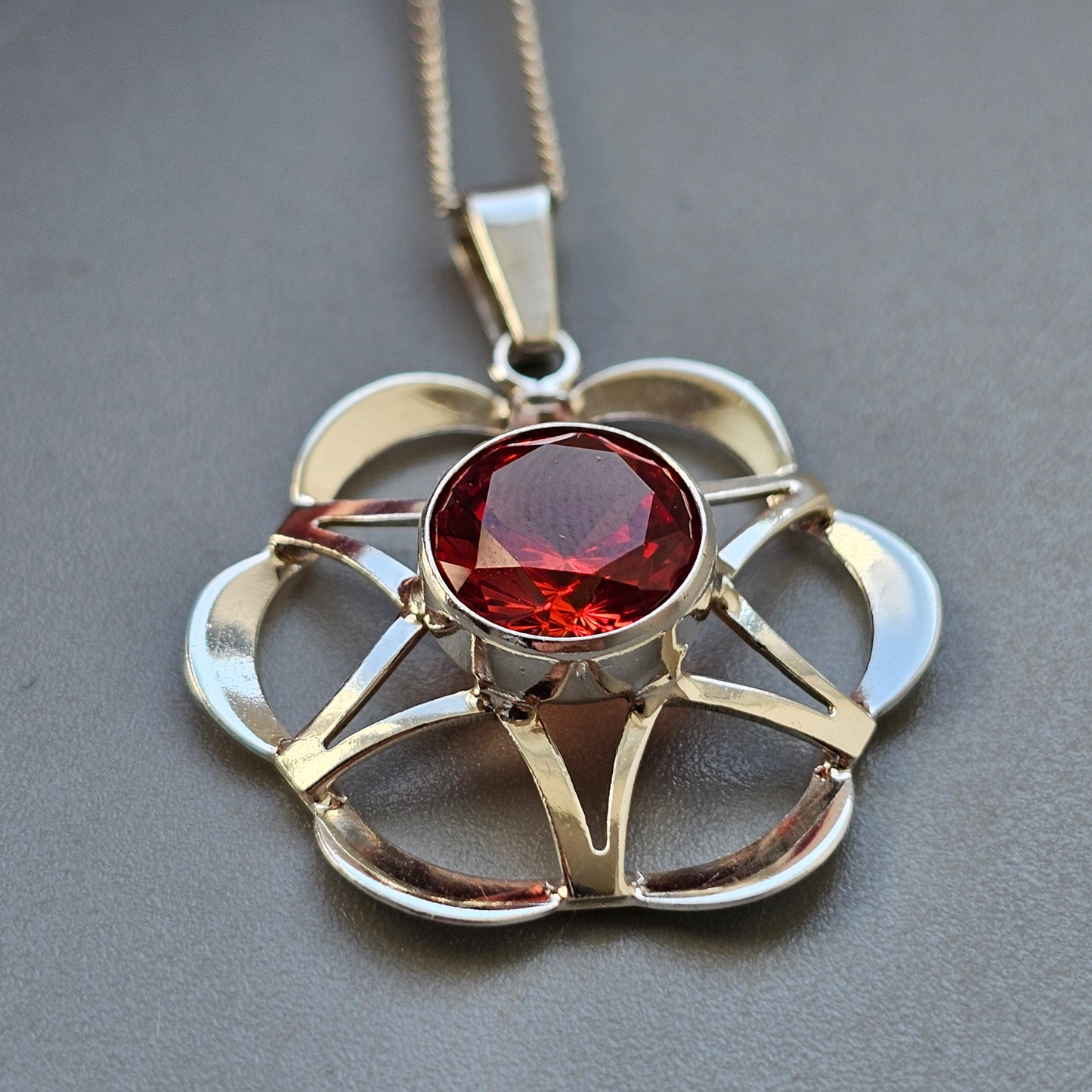 Silver flower-shaped pendant necklace with a central red gemstone.