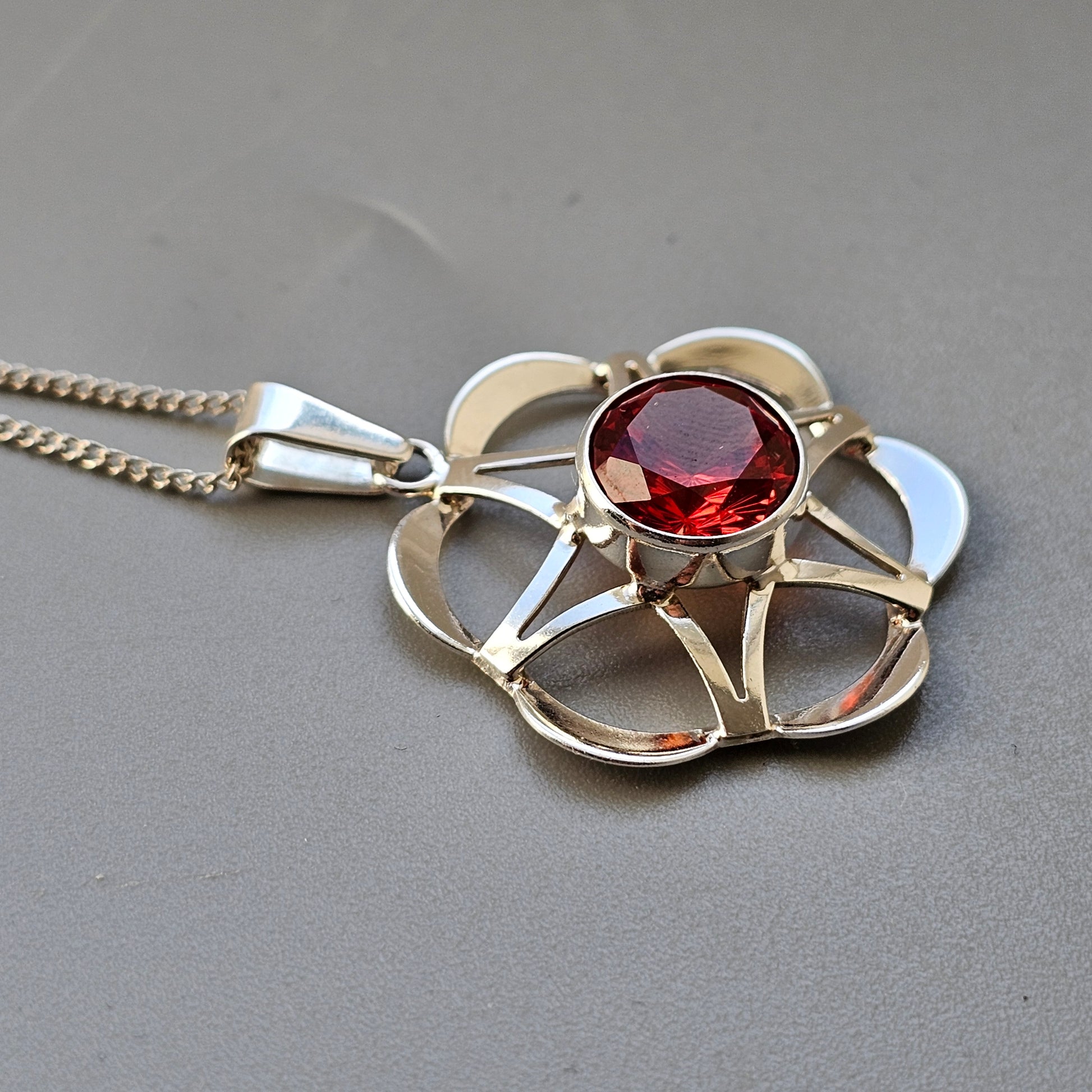 Silver flower-shaped pendant necklace with a red gemstone in the center.