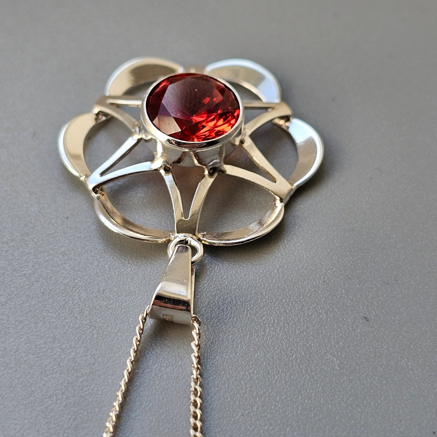 Silver flower-shaped pendant with a central red gemstone.