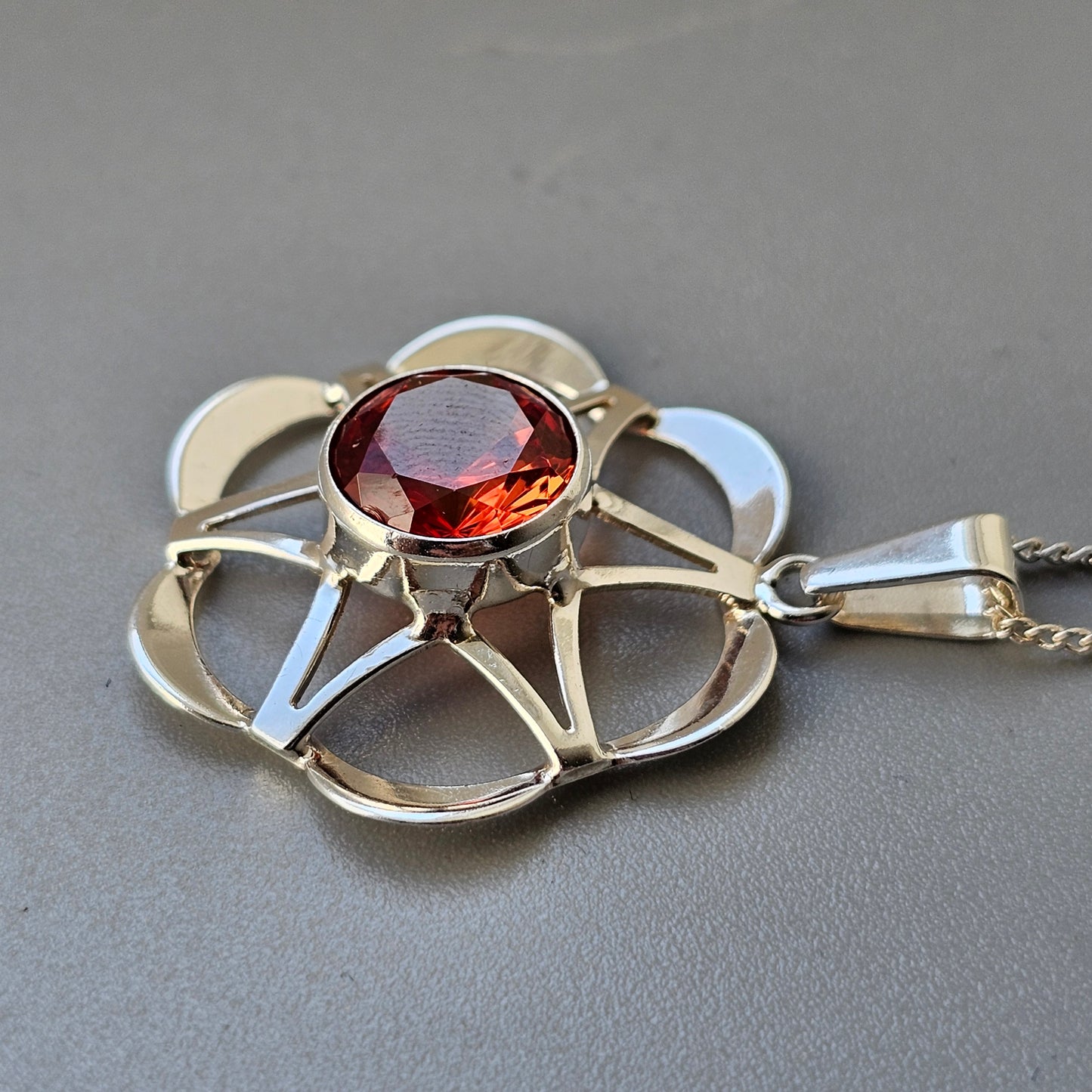 Ornate pendant featuring a red gemstone set in a stylized floral or star-shaped gold frame.