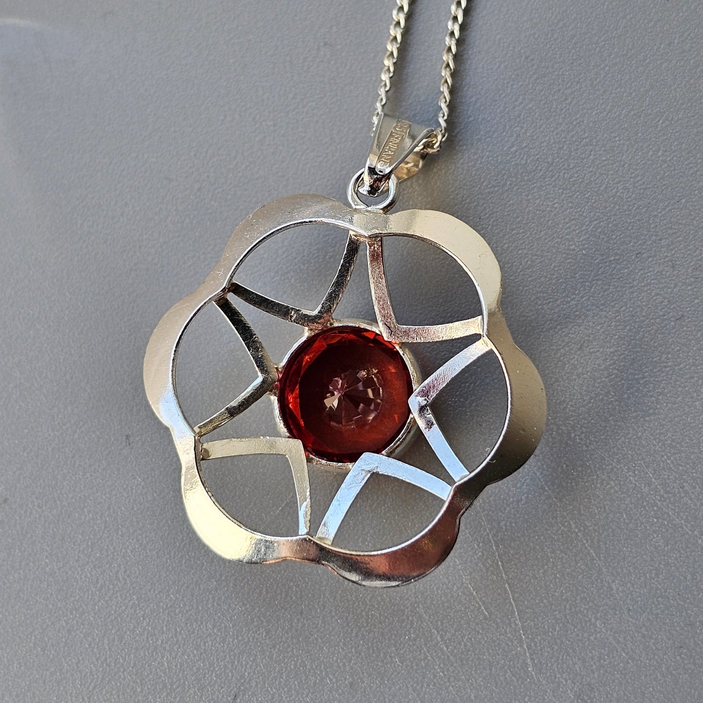 Silver pendant necklace featuring a flower-shaped design with a red gemstone center.