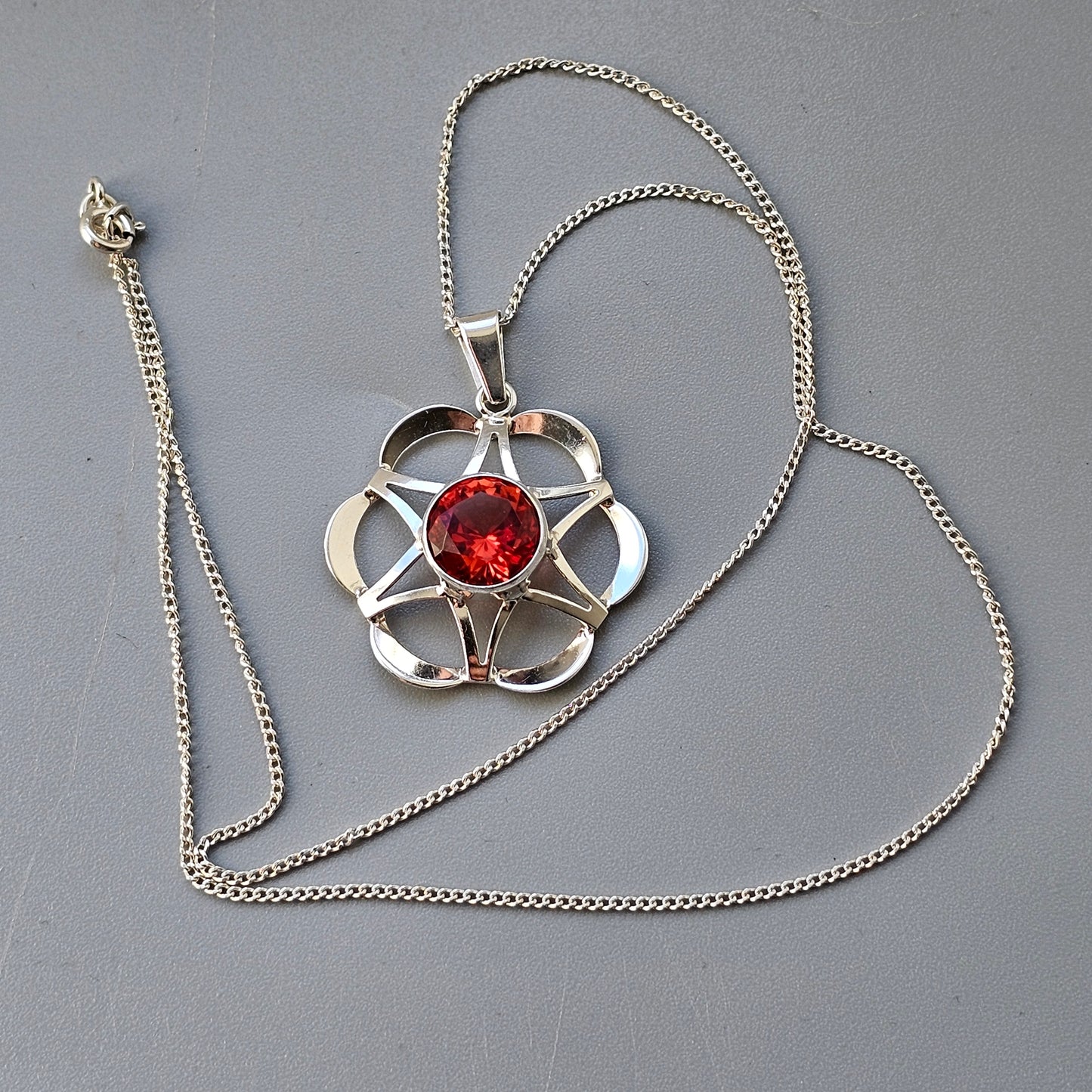 Silver pendant necklace featuring a flower-shaped design with a red gemstone center.