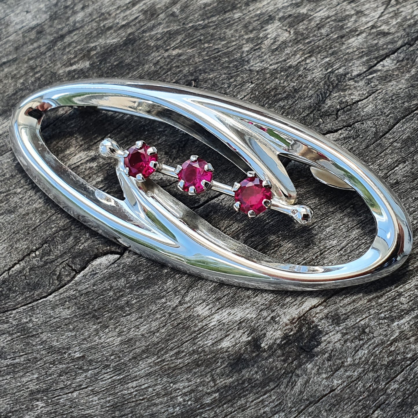 Silver oval brooch with three pink gemstones.