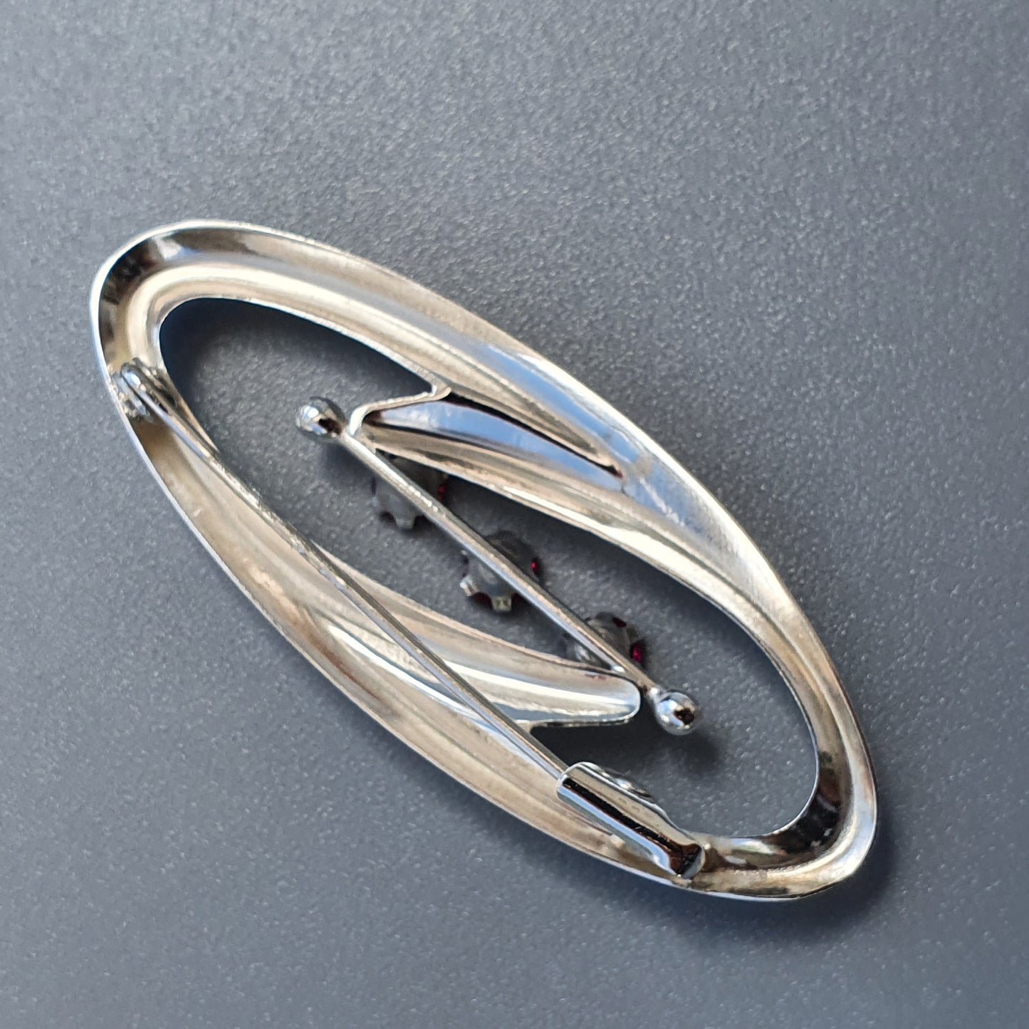 Oval-shaped silver brooch with abstract curved designs and small spherical accents.