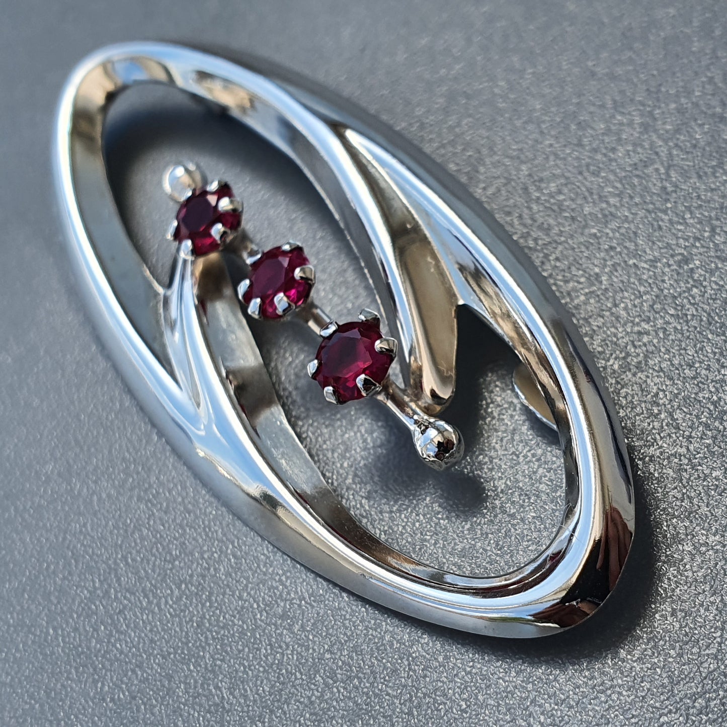 Oval-shaped silver brooch featuring three small red gemstones.