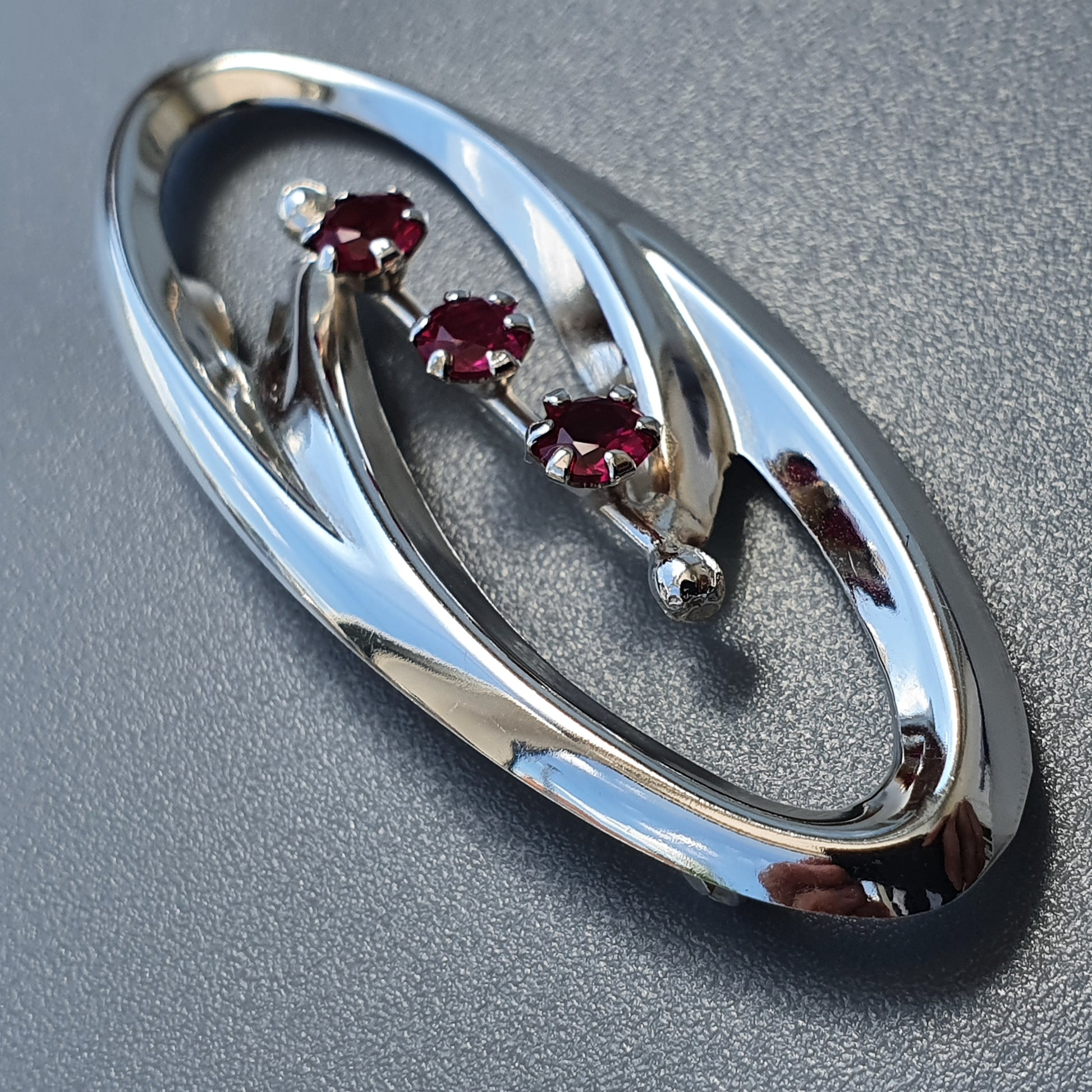 Oval-shaped silver brooch with three small red gemstones.