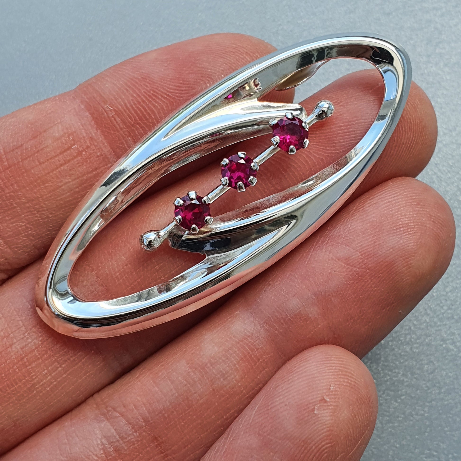 Oval-shaped silver brooch with three small red gemstones.