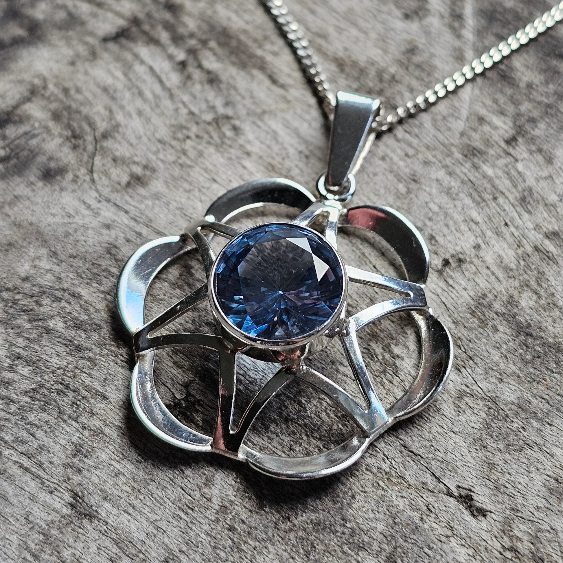 Silver flower-shaped pendant necklace with a blue gemstone center.