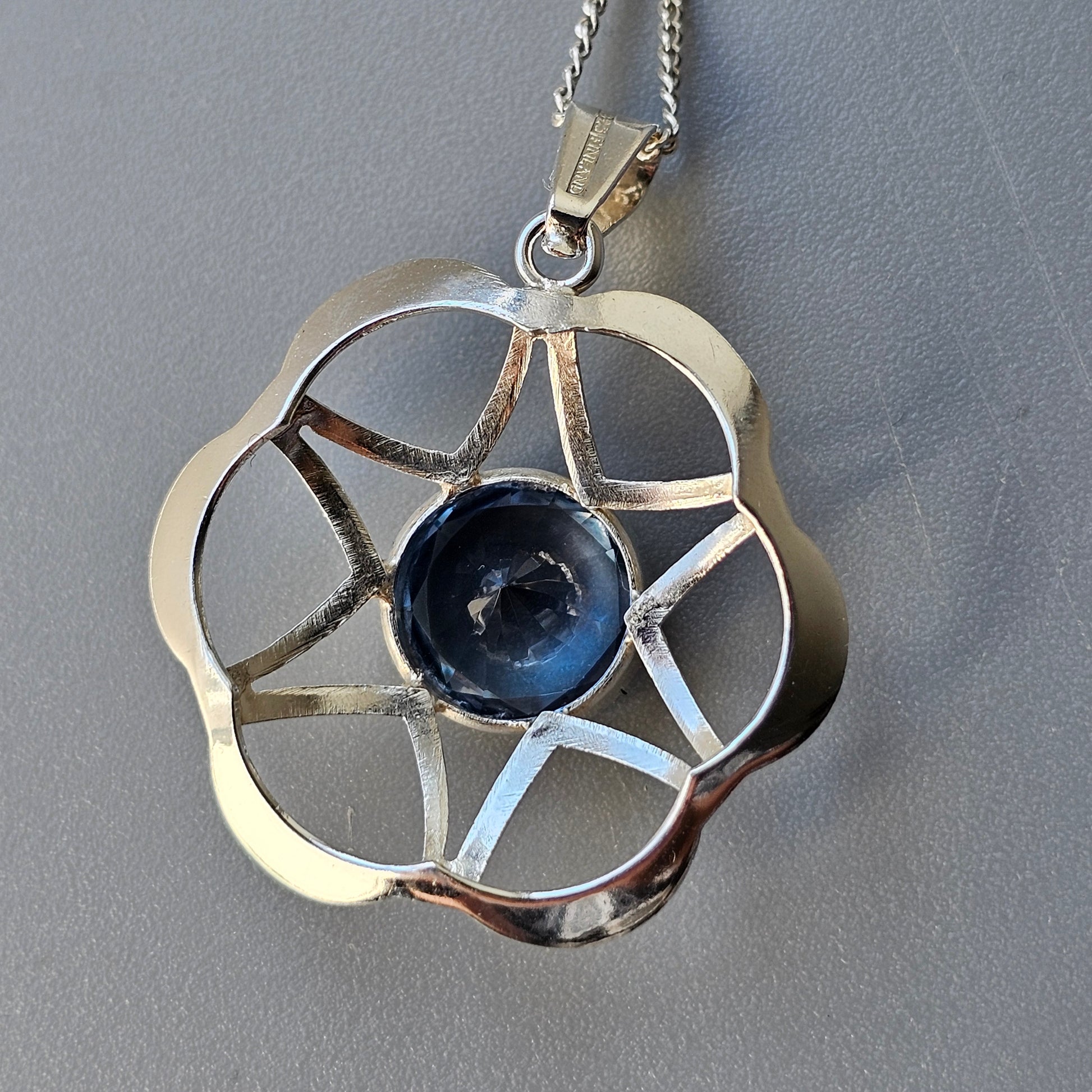 Silver pendant necklace with a flower-shaped design and a blue gemstone center.