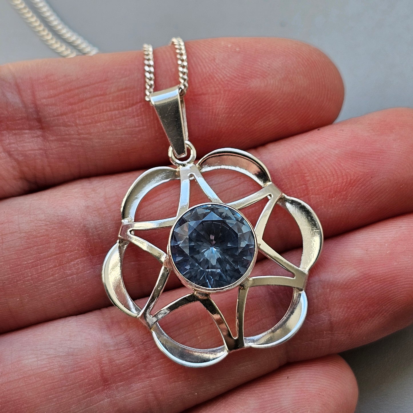 Silver pendant necklace featuring a flower-shaped design with a blue gemstone at its center.