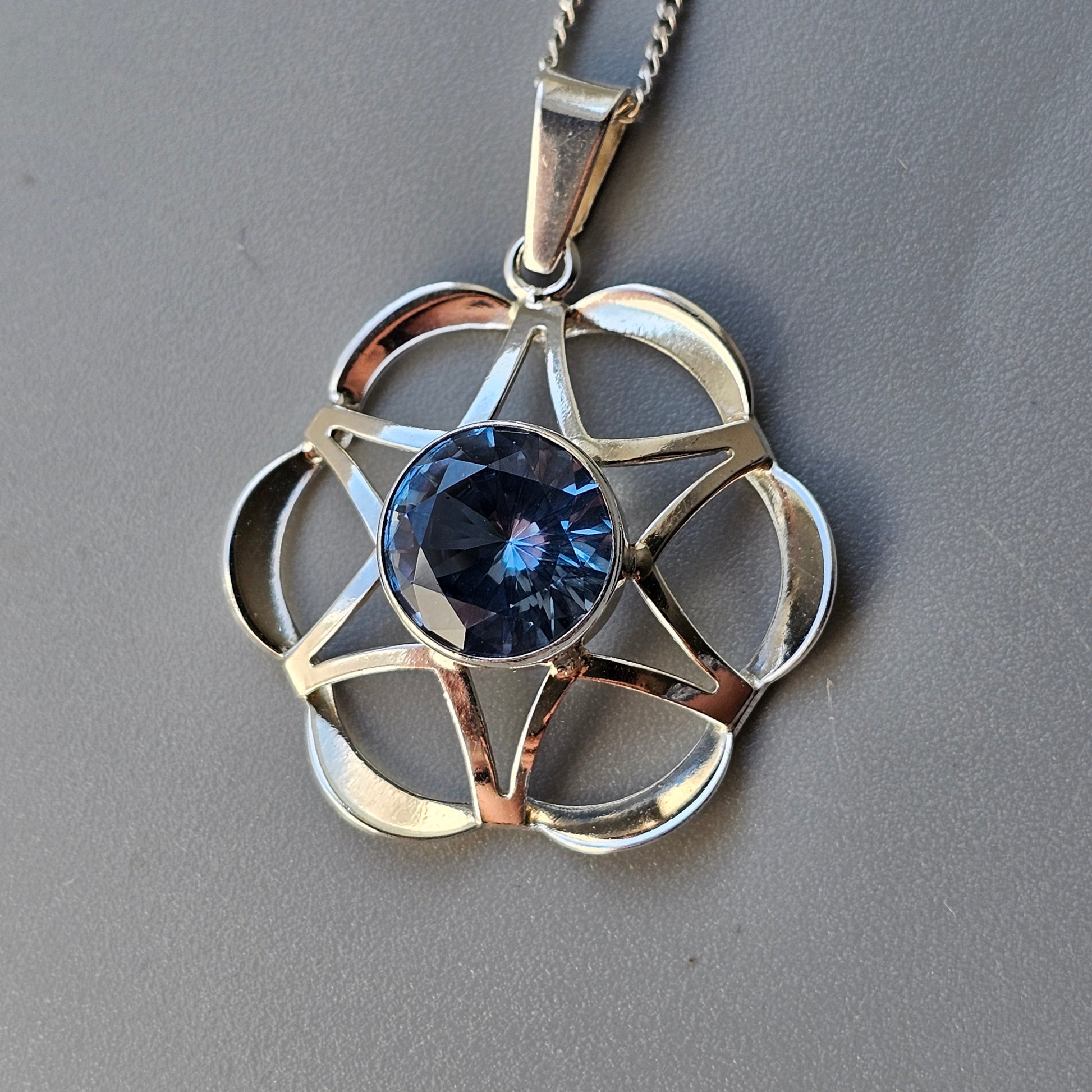 Silver pendant necklace featuring a blue gemstone set within a floral or star-shaped design.