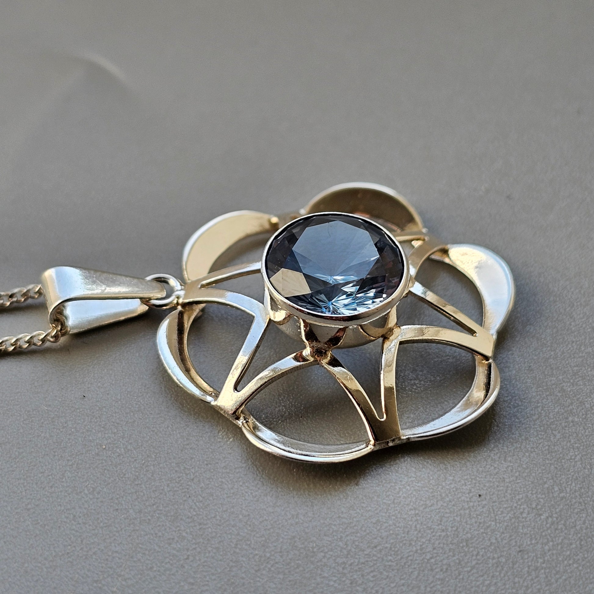 Floral-shaped silver pendant with a blue gemstone center.