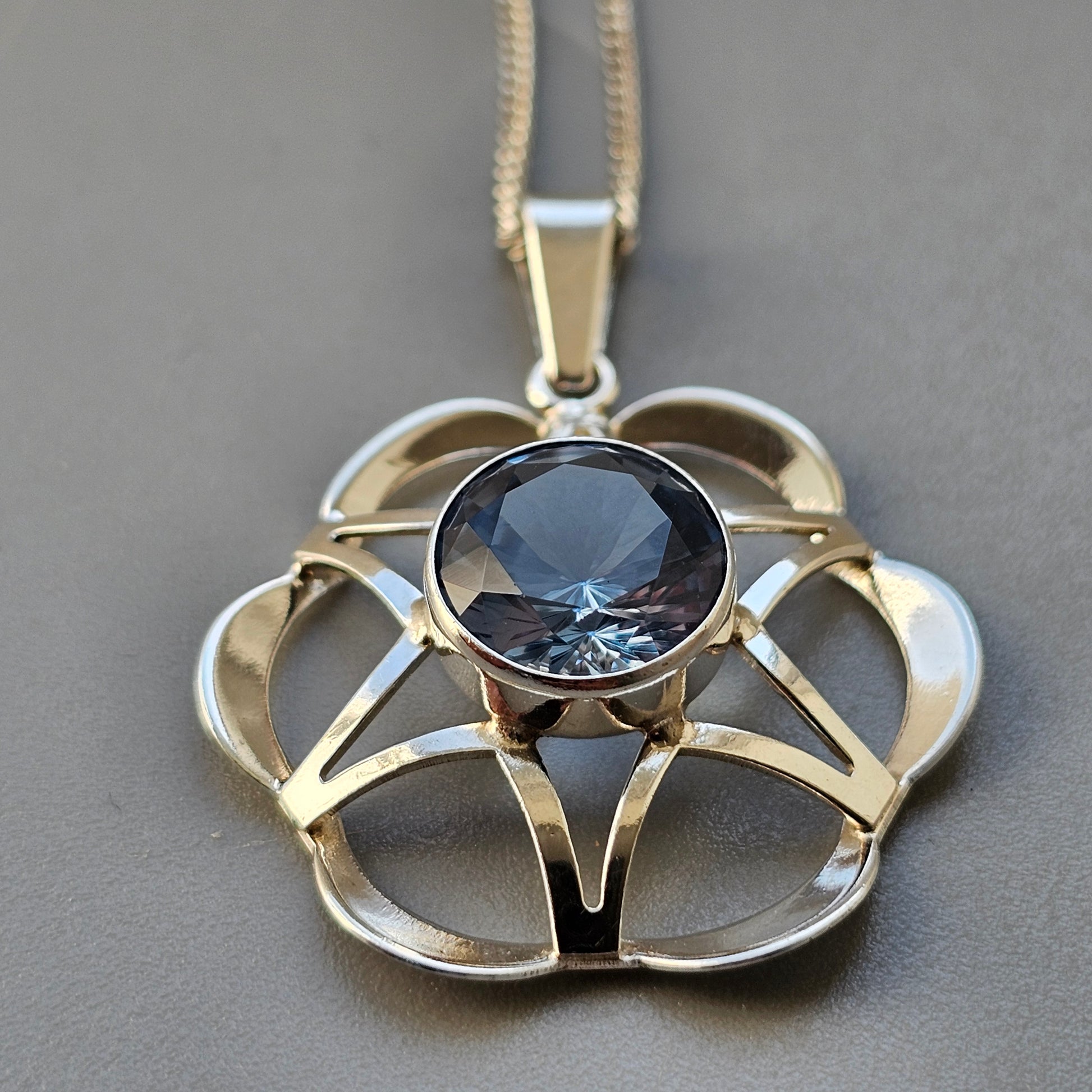 Ornate gold and silver pendant necklace featuring a blue gemstone centerpiece in a floral-inspired design.