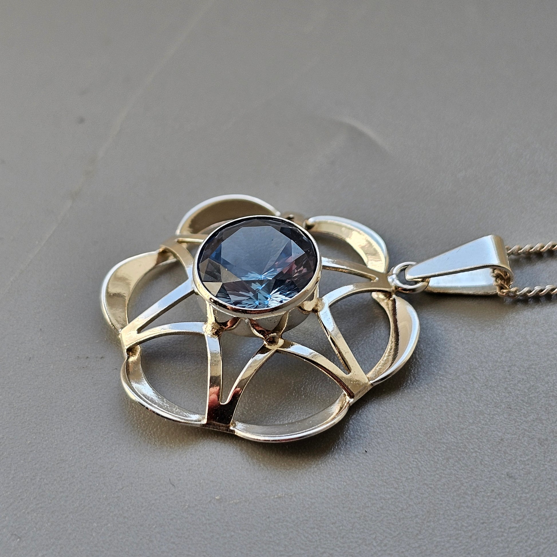 Flower-shaped silver pendant with a blue gemstone center.