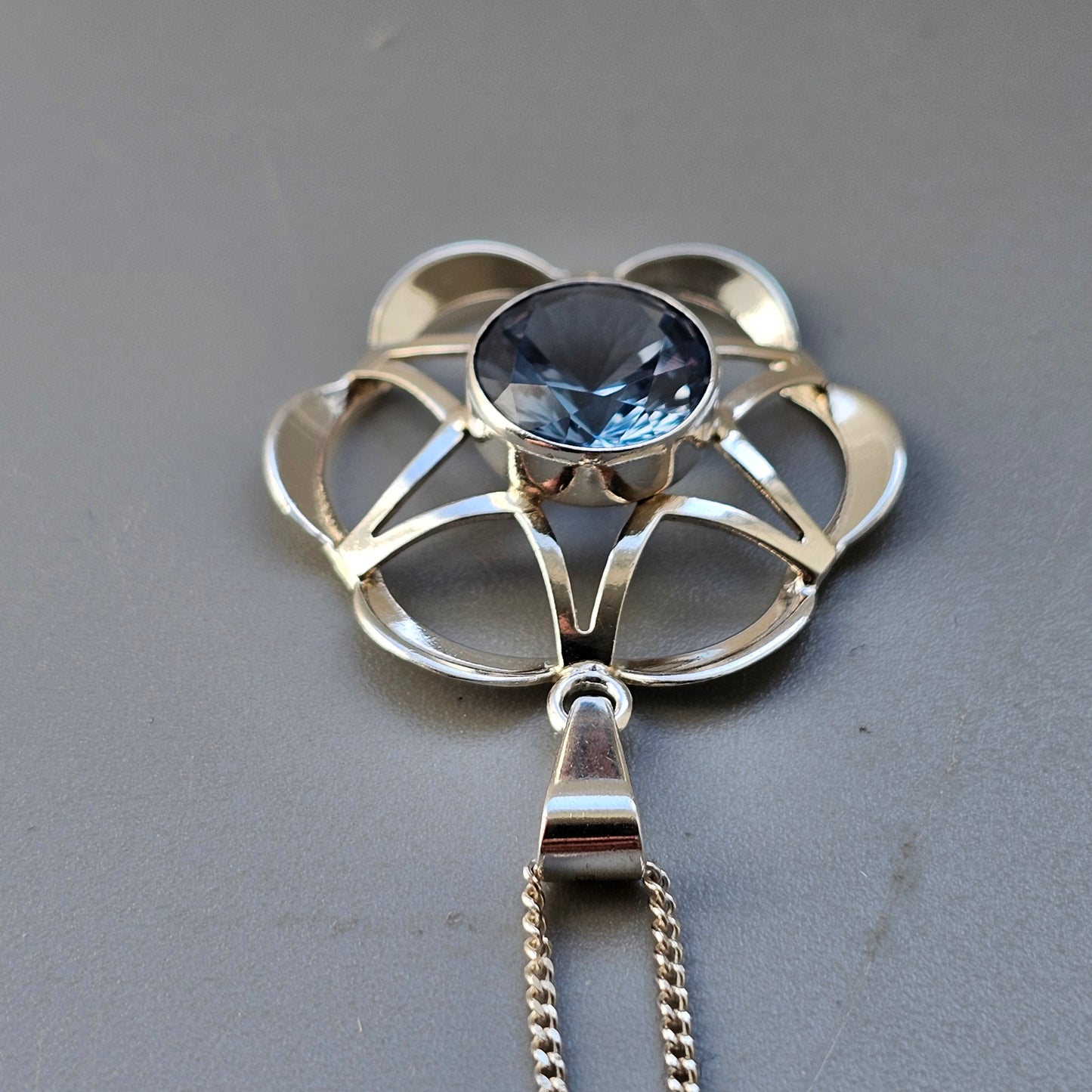 Silver pendant featuring a flower-like design with a central blue gemstone.