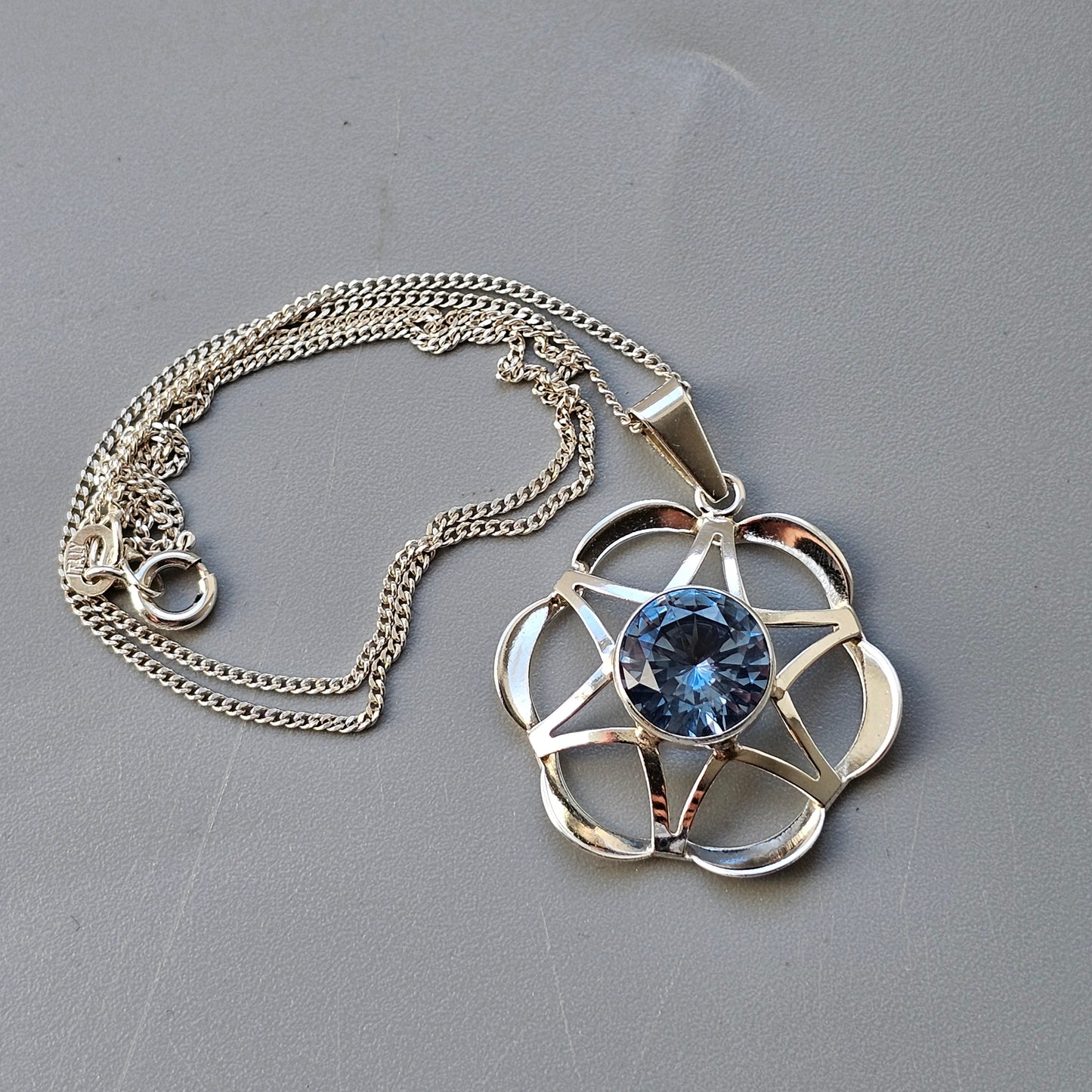 Silver pendant necklace featuring a flower-shaped design with a blue gemstone center.