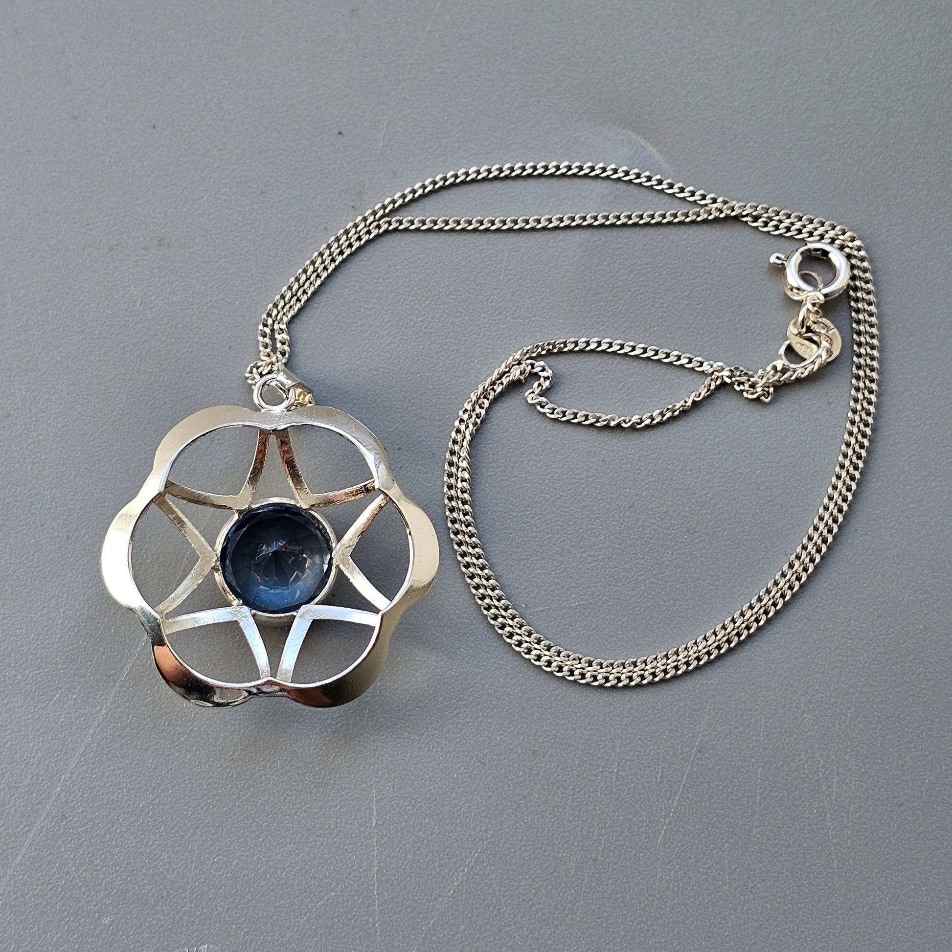 Silver pendant necklace featuring a geometric star design with a blue gemstone in the center.