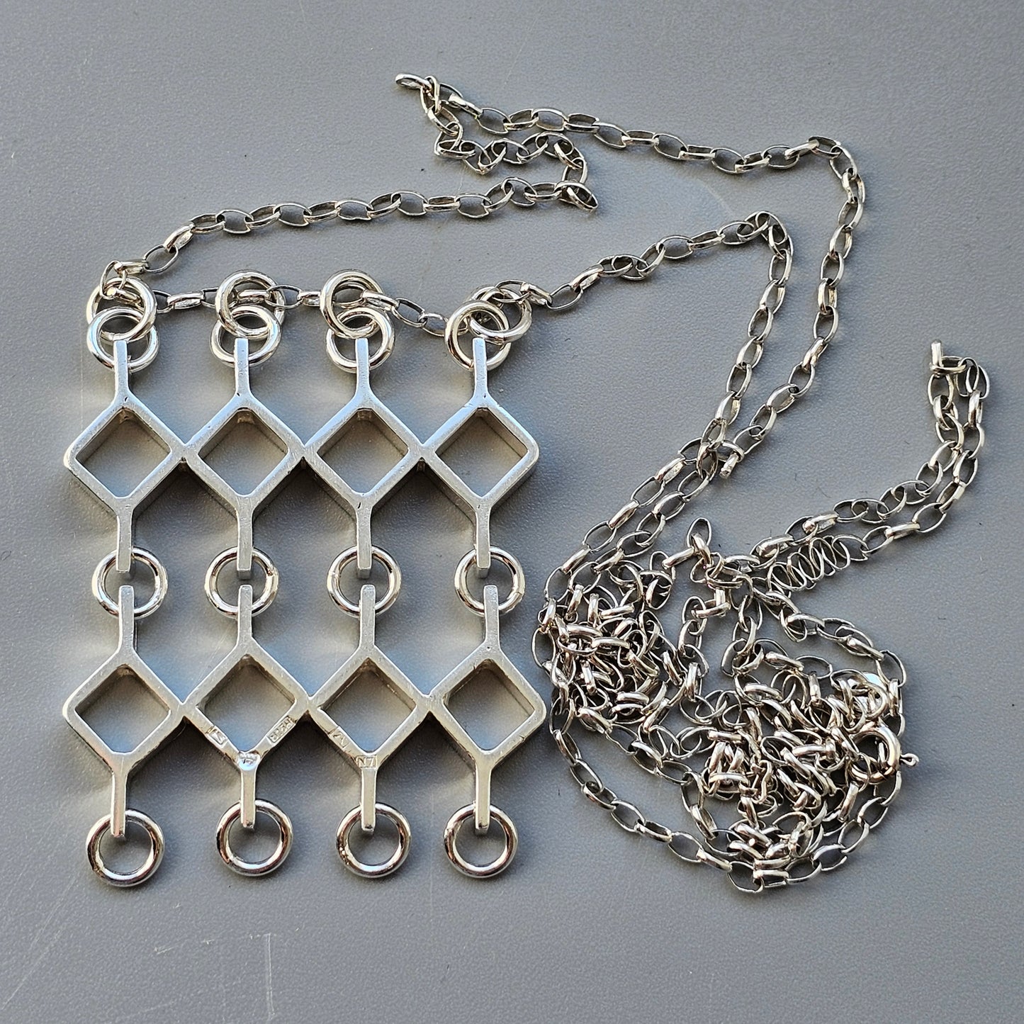 Silver necklace with a geometric pendant featuring interconnected diamond shapes and rings.