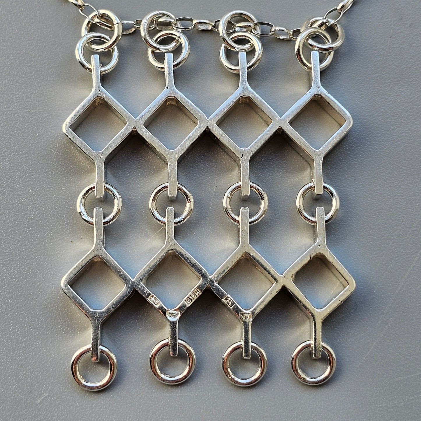 Silver geometric pendant necklace with interconnected diamond shapes and rings.