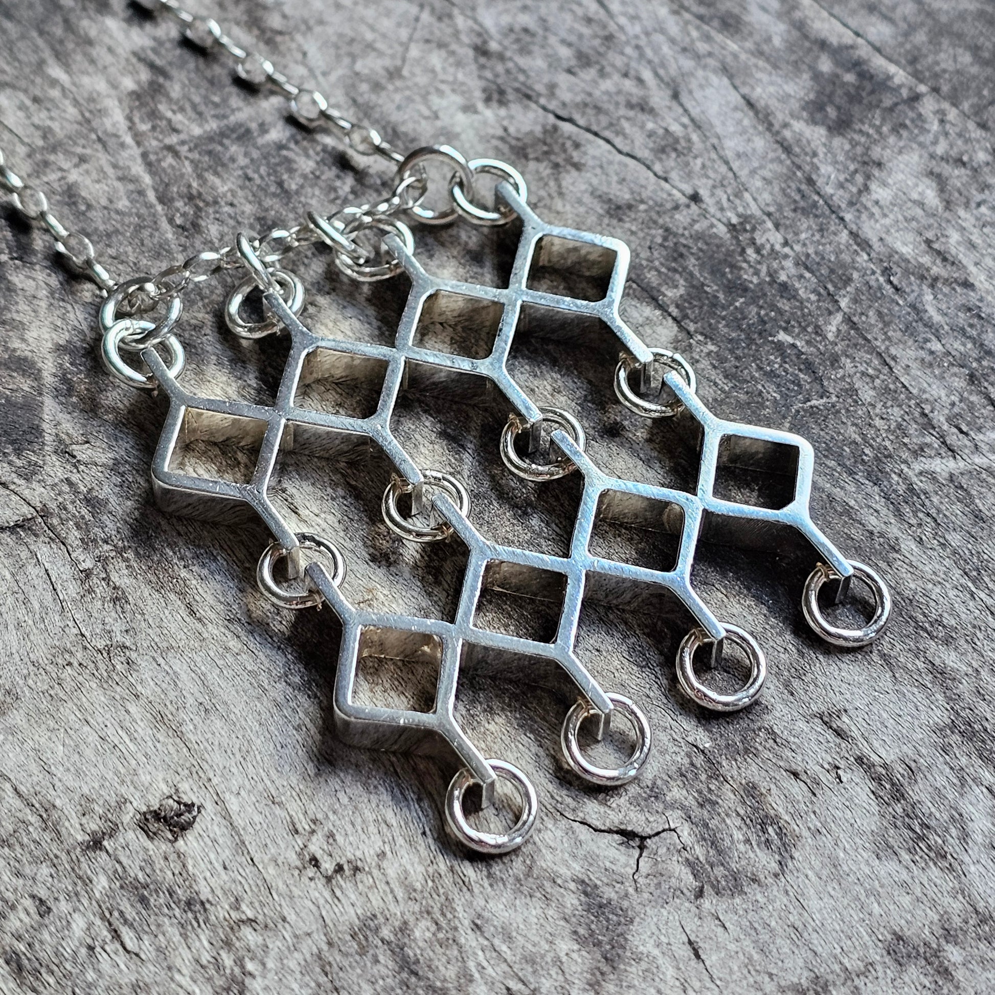 Geometric silver pendant necklace with interconnected square shapes and circular attachments.