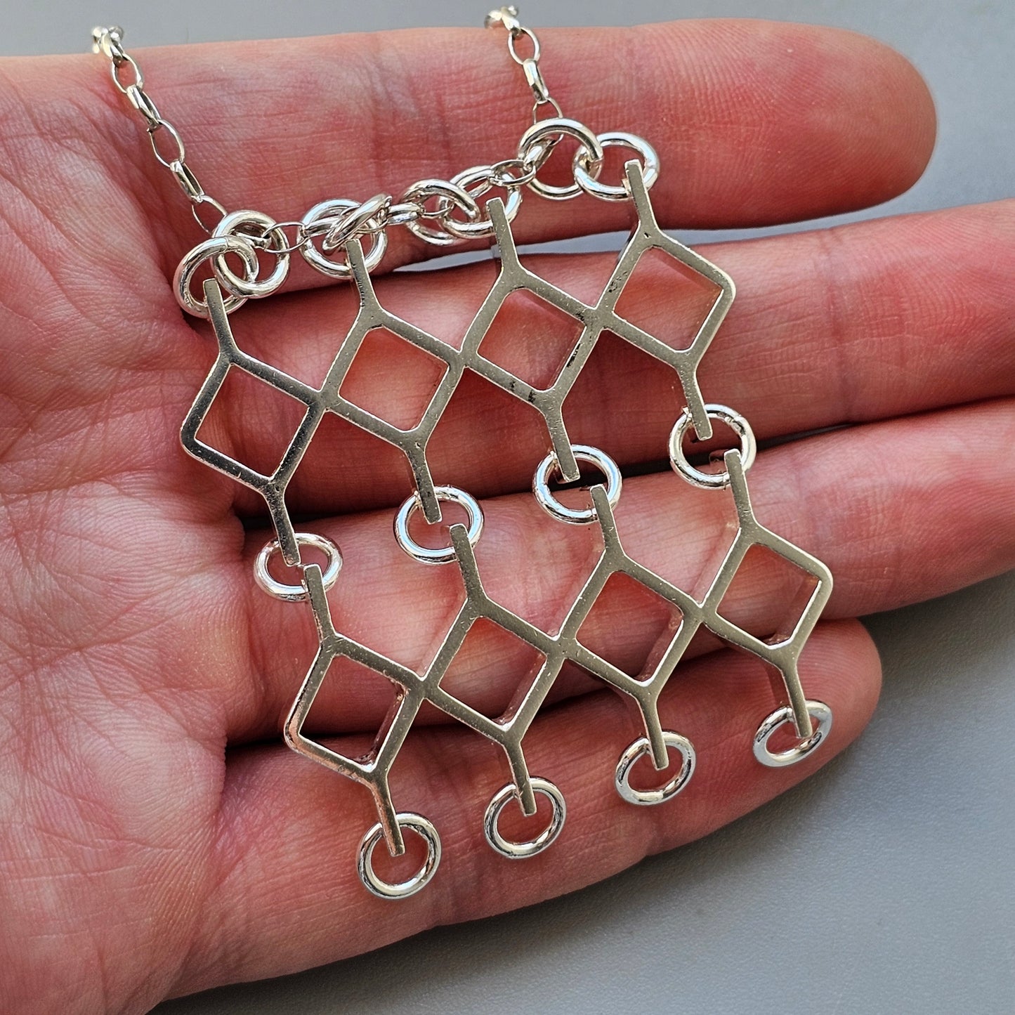 Silver geometric pendant necklace with interconnected squares and circles.