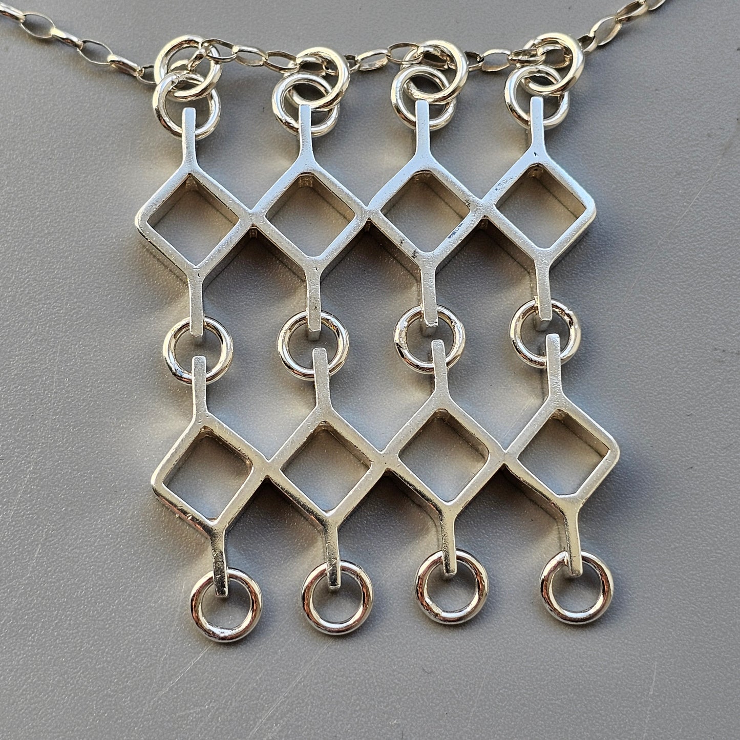 Silver necklace with a geometric diamond-shaped pattern pendant.