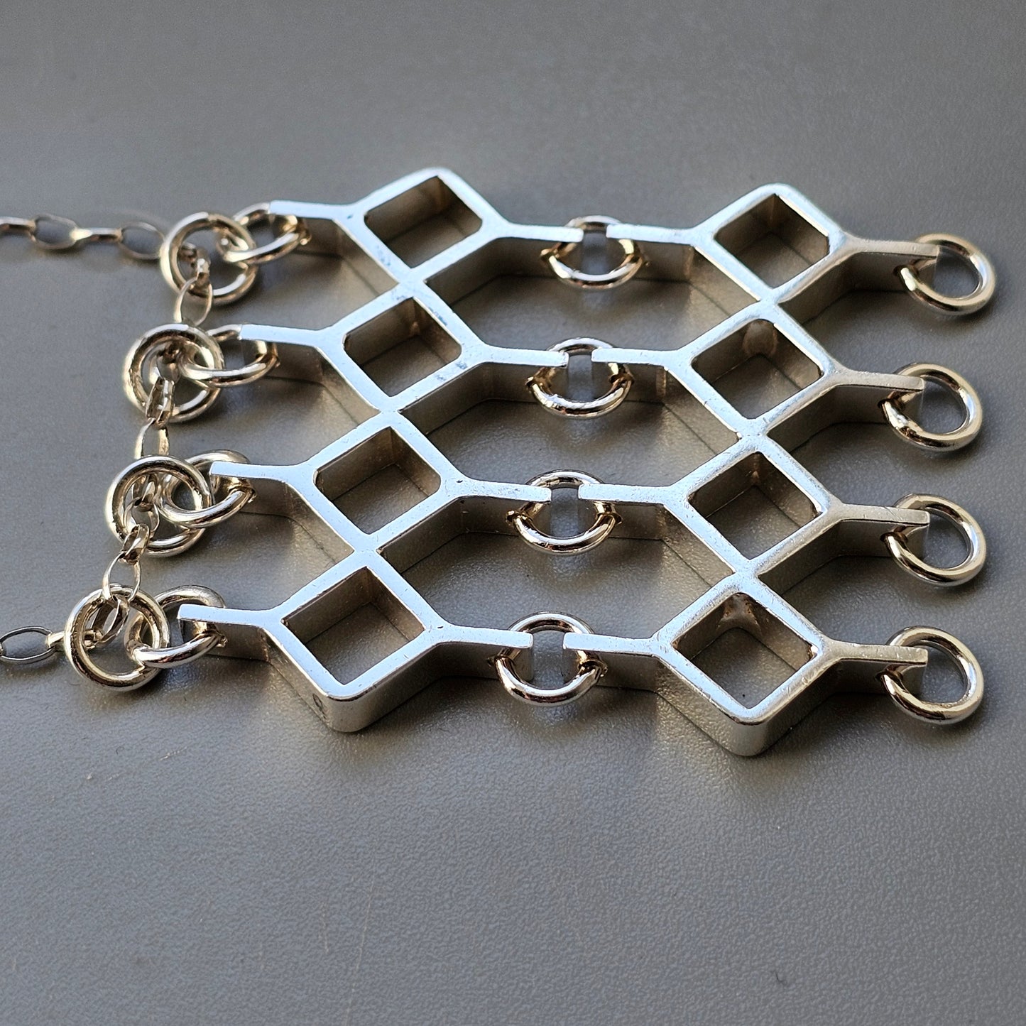 Geometric silver-toned metal jewelry piece with diamond-shaped links and small rings.