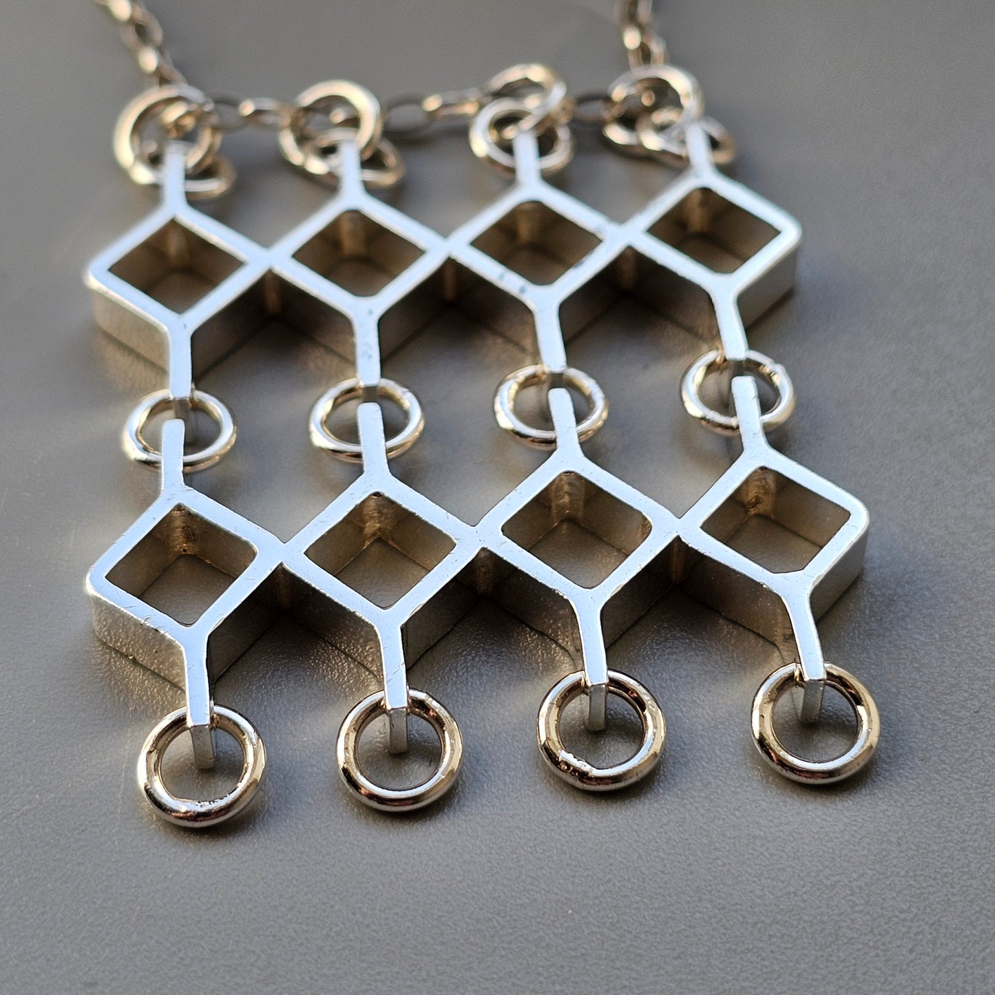 Geometric silver pendant with diamond-shaped links and small rings attached.