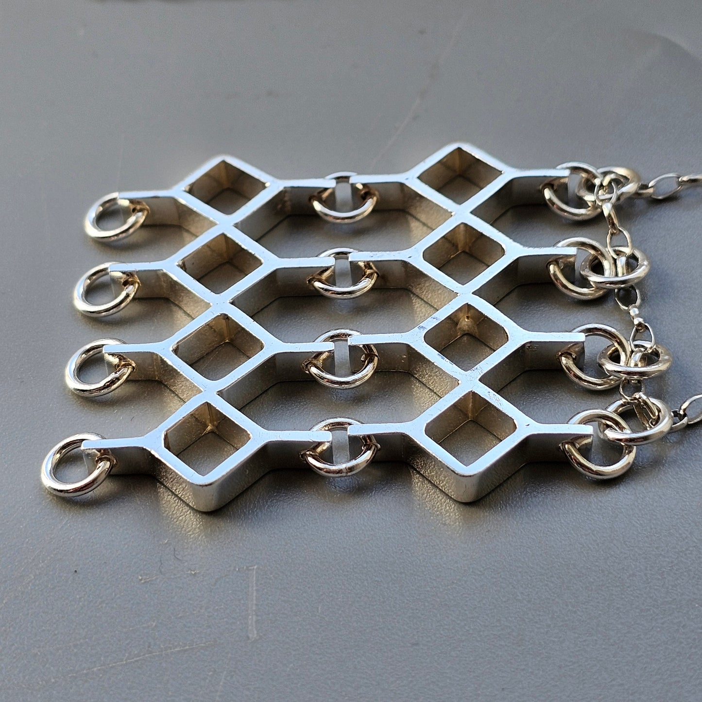 Metallic lattice-like jewelry piece with diamond-shaped openings and attached rings.