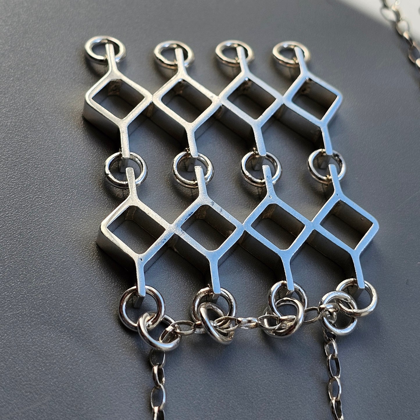 Silver geometric pendant necklace with interconnected diamond shapes.