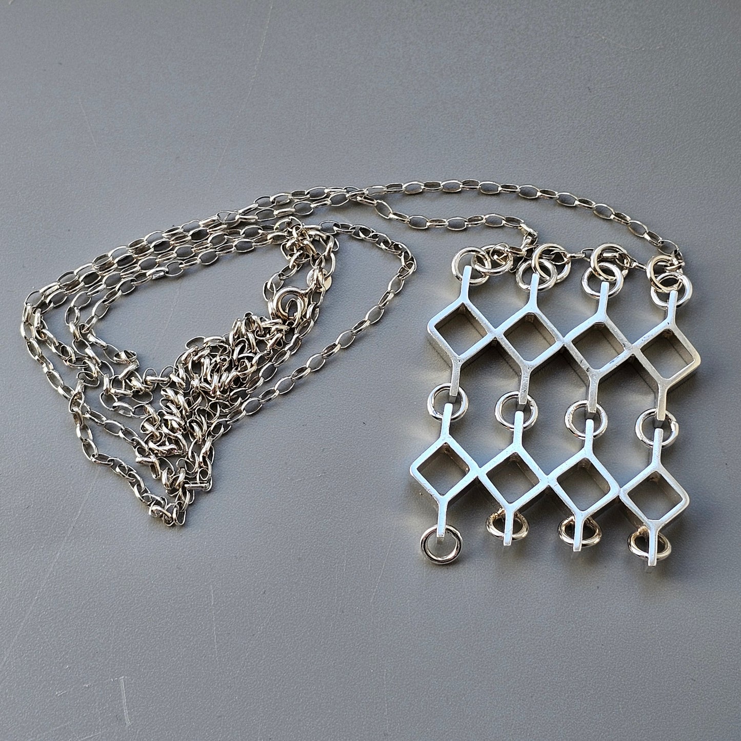 Silver geometric pendant necklace with interconnected diamond shapes.