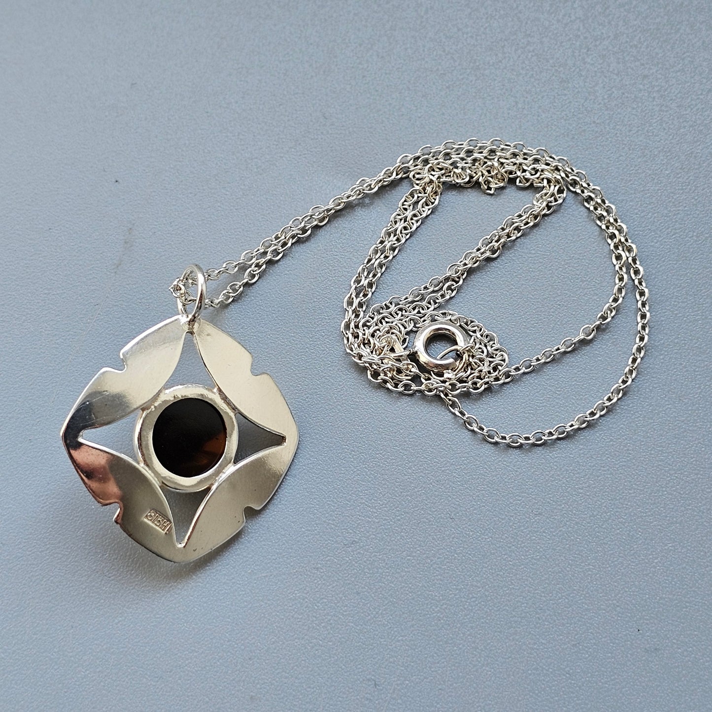 Silver pendant necklace with an abstract, curved design and a dark circular center.