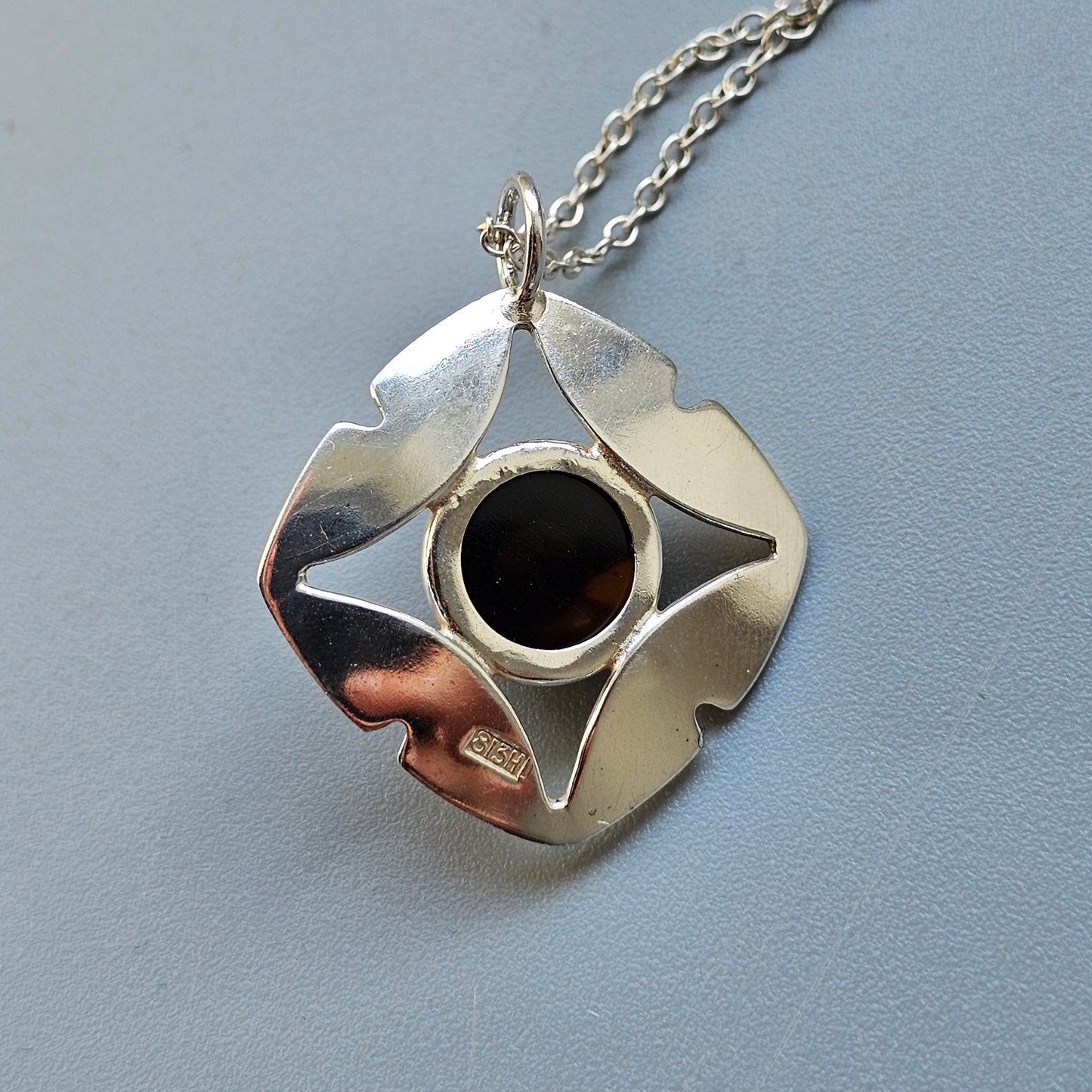 Silver pendant necklace with a circular black center and petal-like metallic shapes surrounding it.