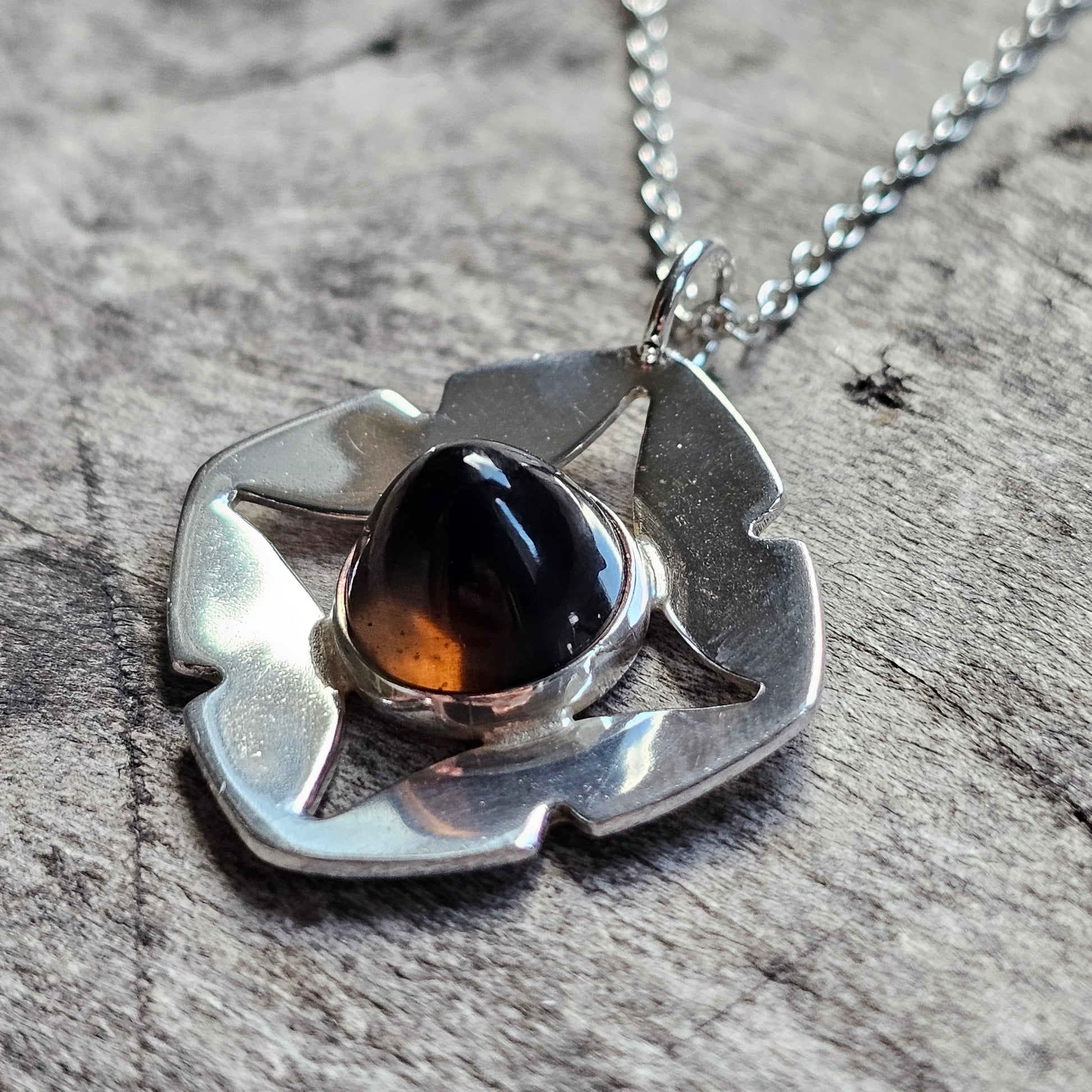 Silver pendant necklace featuring a stylized flower shape with a dark amber gemstone center.