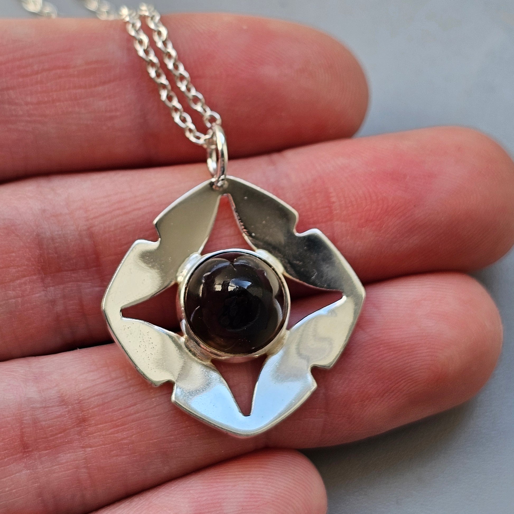 Silver pendant necklace featuring a dark spherical stone set within a stylized flower-shaped design.