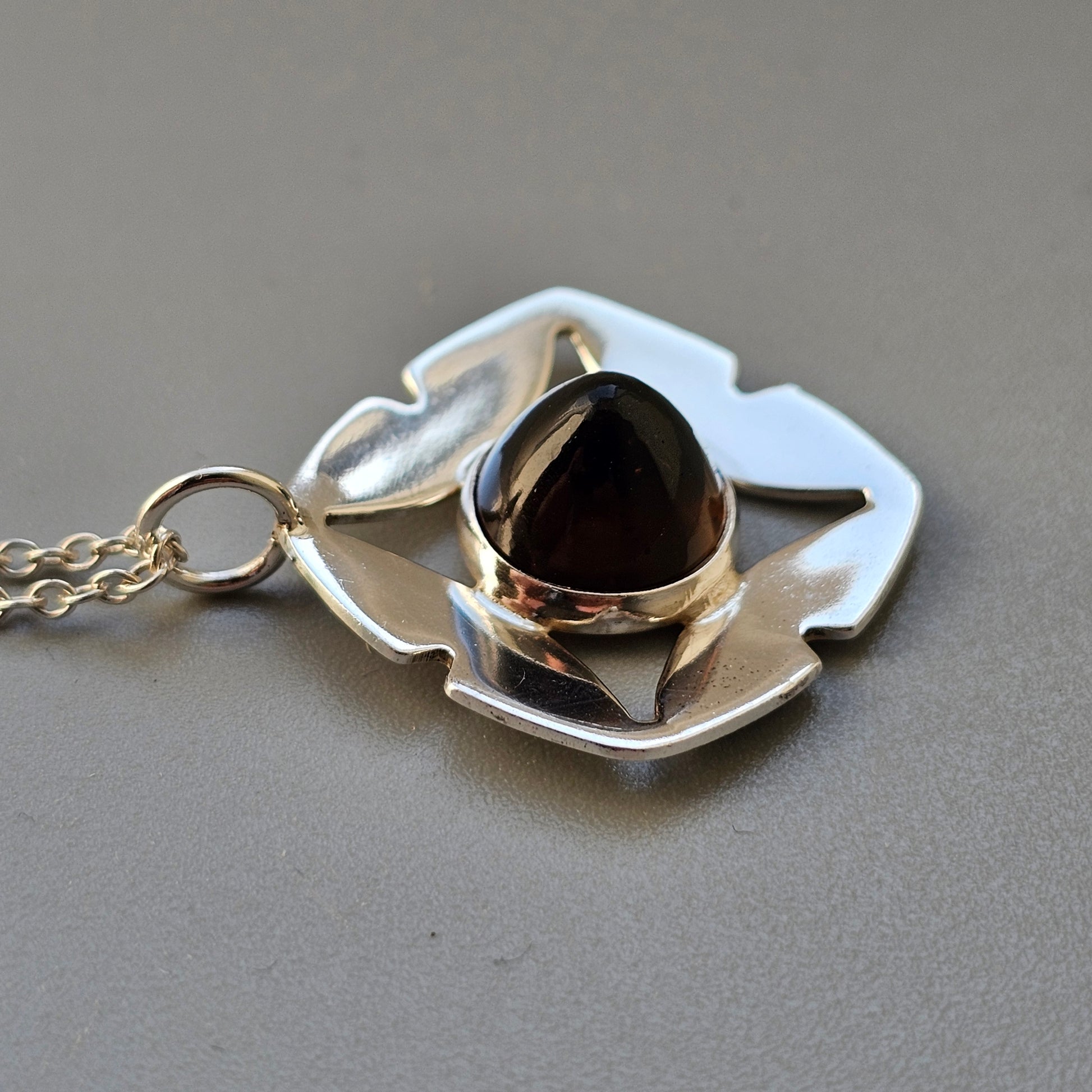 Silver pendant necklace featuring a stylized leaf or petal shape with a dark stone set in the center.