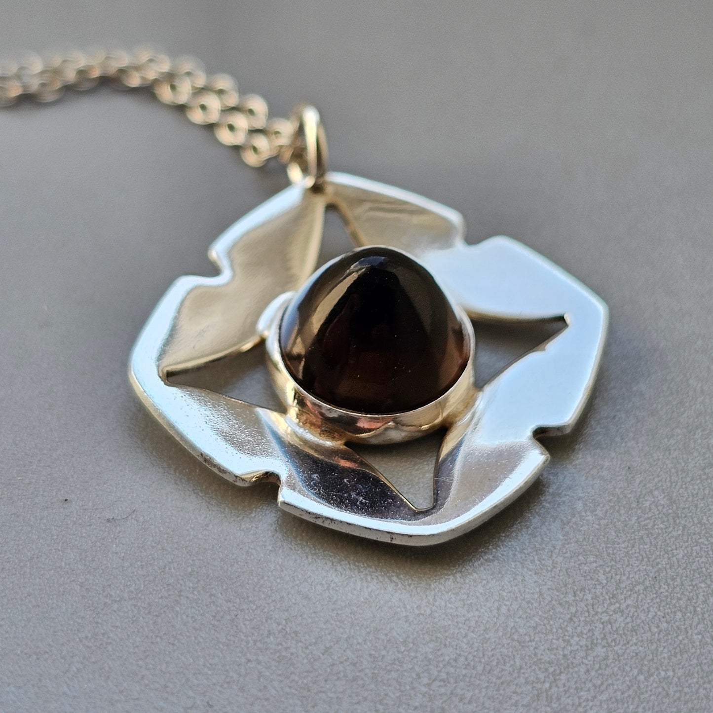 Silver pendant necklace featuring an abstract flower design with a dark gemstone center.