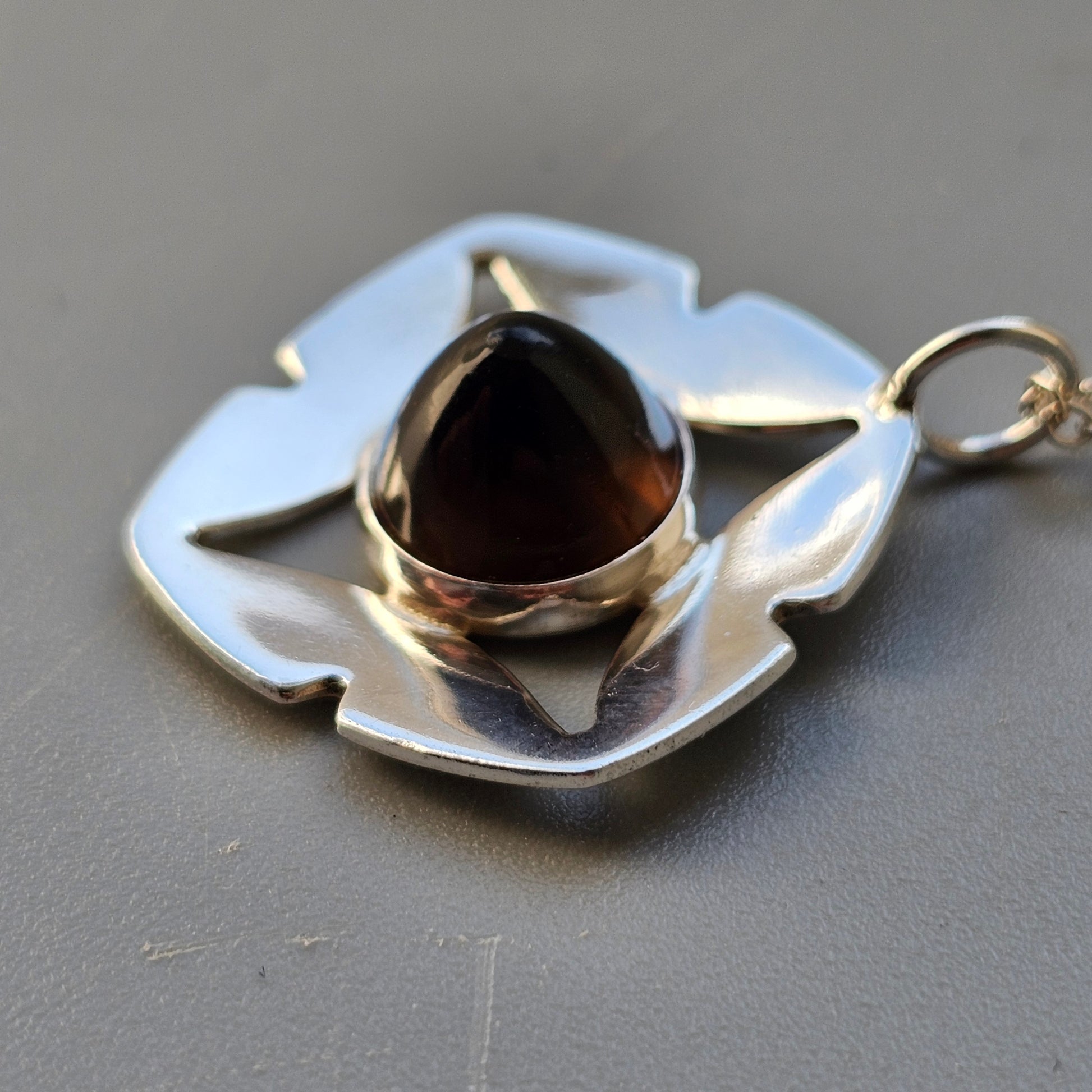 Leaf-shaped silver pendant with a dark gemstone at its center.