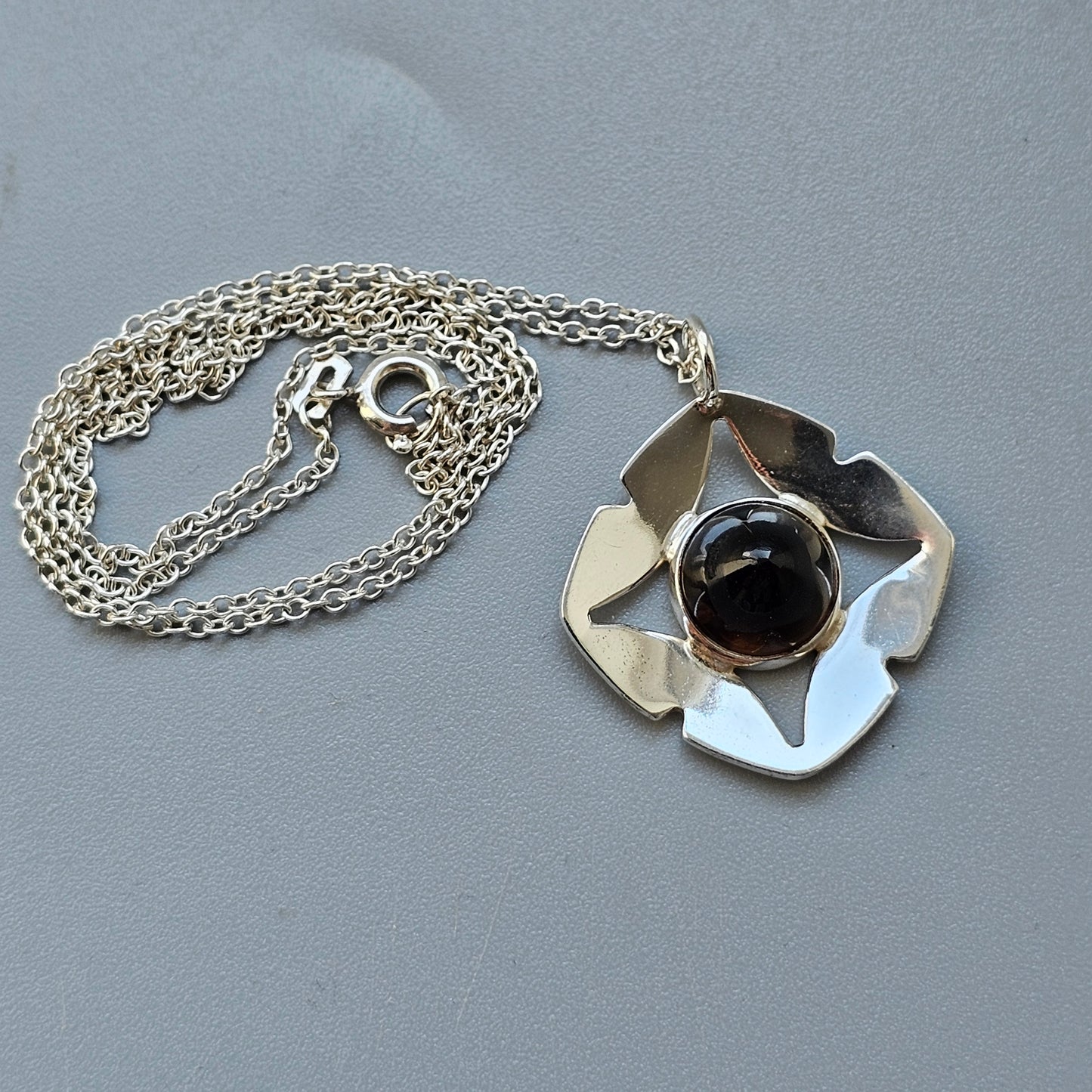 Silver pendant necklace with an abstract flower-like design and a dark gemstone center.