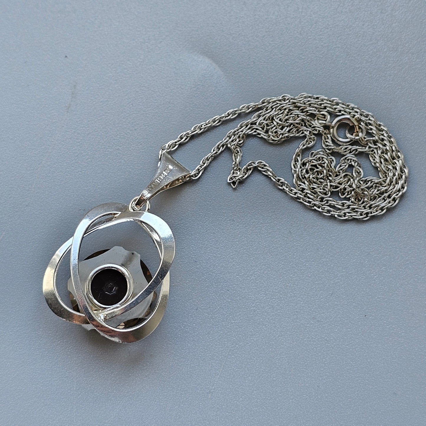 Silver pendant necklace with an interlocking circular design and a dark stone in the center.