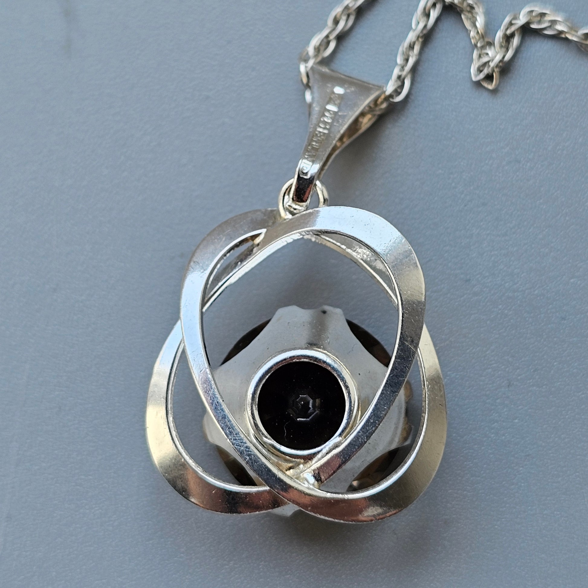 Silver pendant necklace with an interlocking triquetra-like design and a dark center stone.