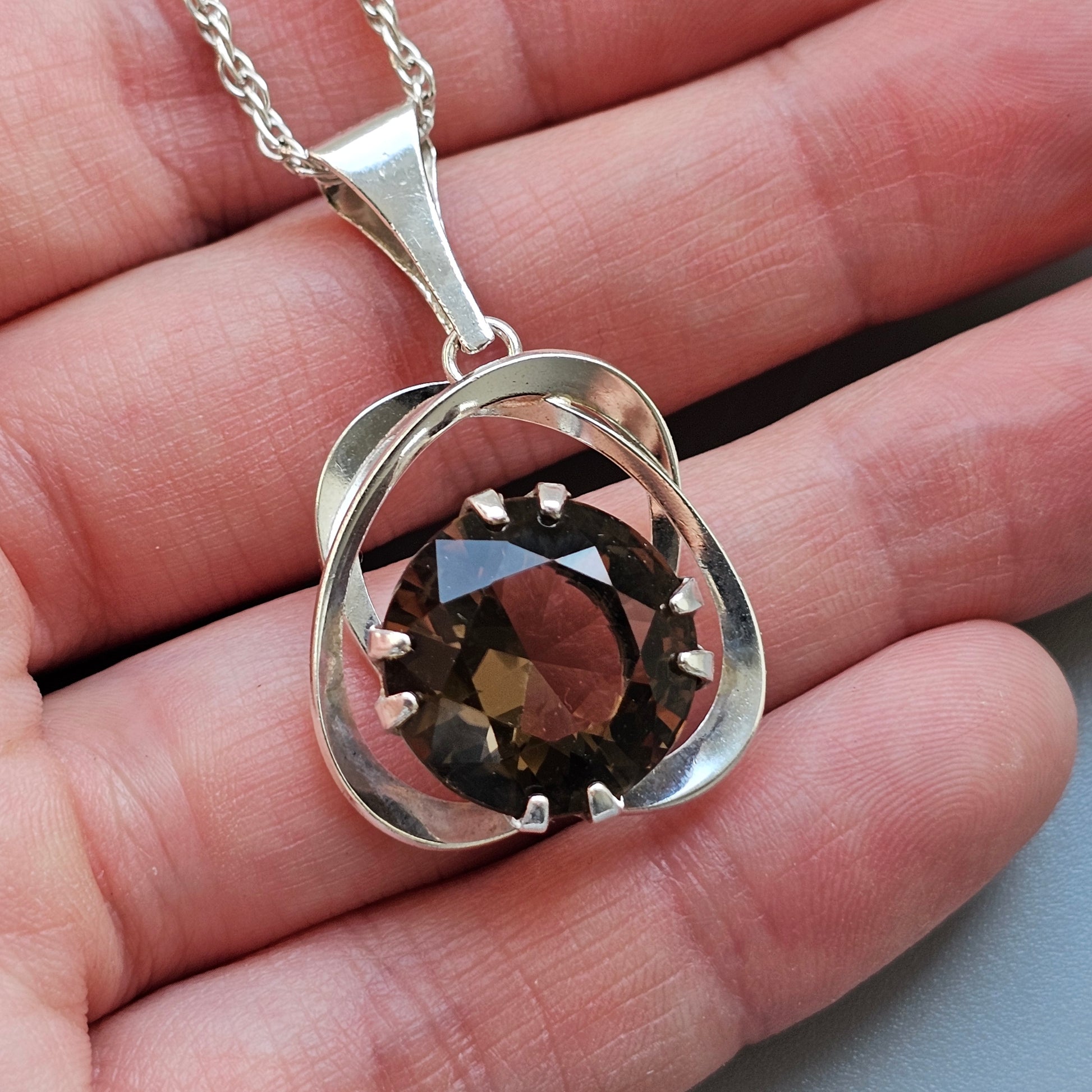 Silver pendant necklace featuring a smoky quartz gemstone encircled by a twisted metal design.