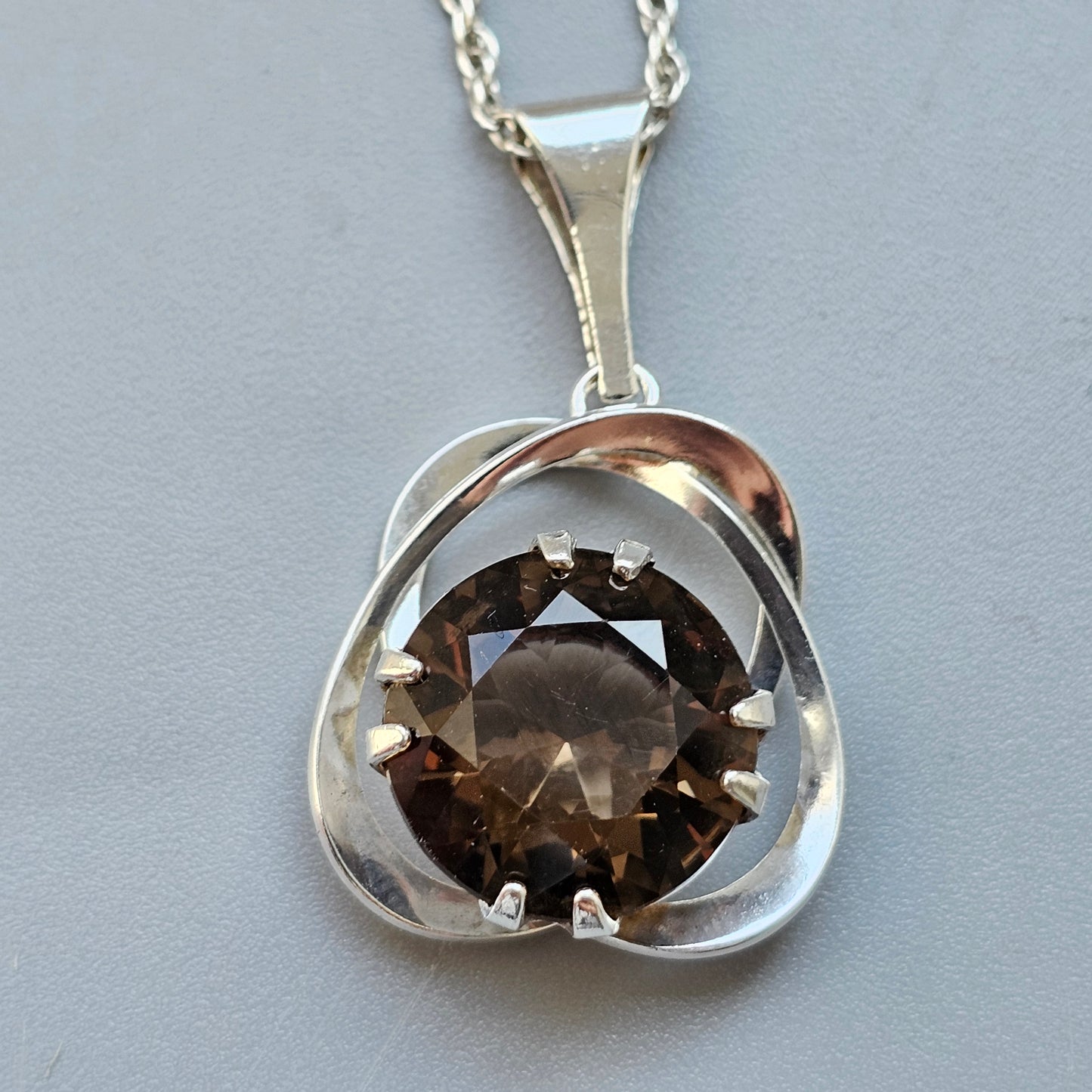 Silver pendant necklace featuring a round brown gemstone set in a curved, abstract design.