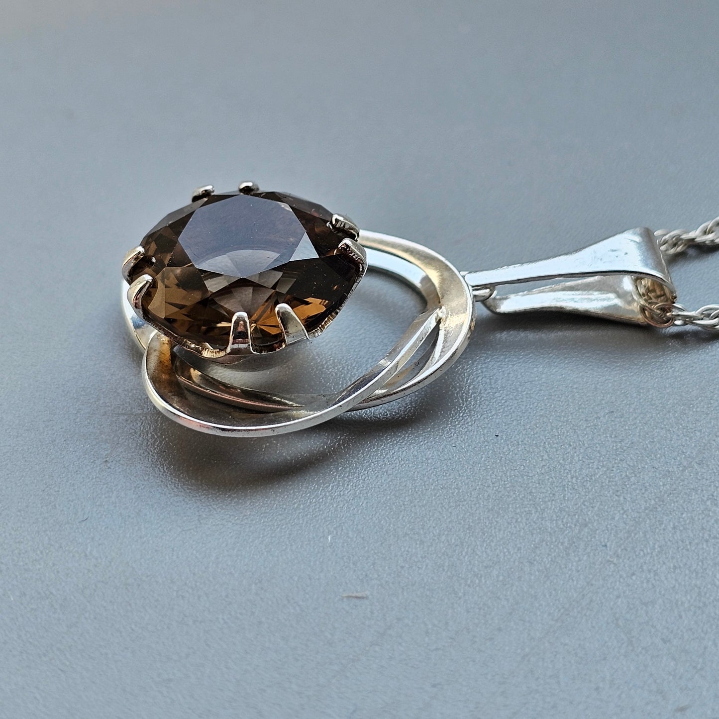 Silver pendant necklace featuring a brown gemstone set in a swirling design.