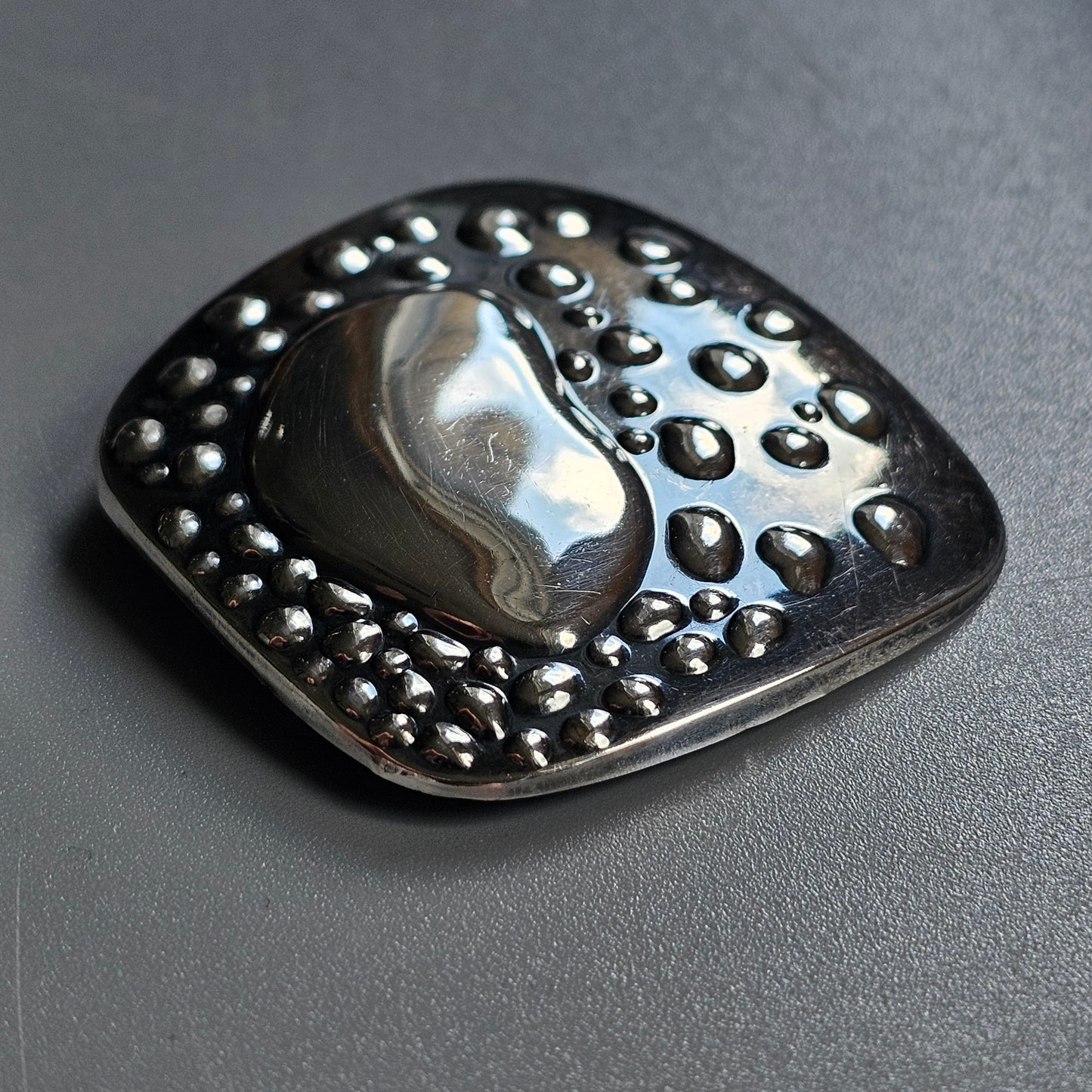 Metallic brooch or pendant with a yin-yang design and dotted textures.