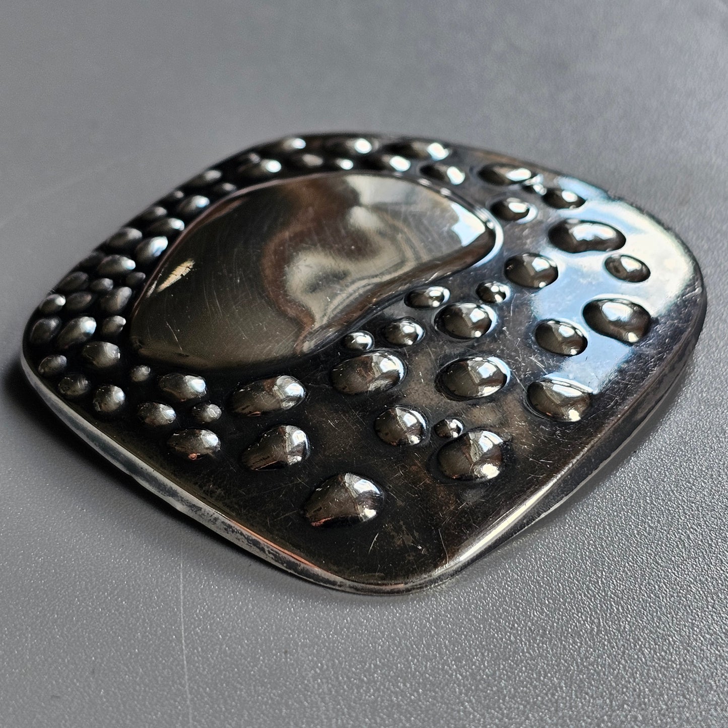 Metallic pendant with a teardrop-shaped center and bubble-like embellishments around the edges.