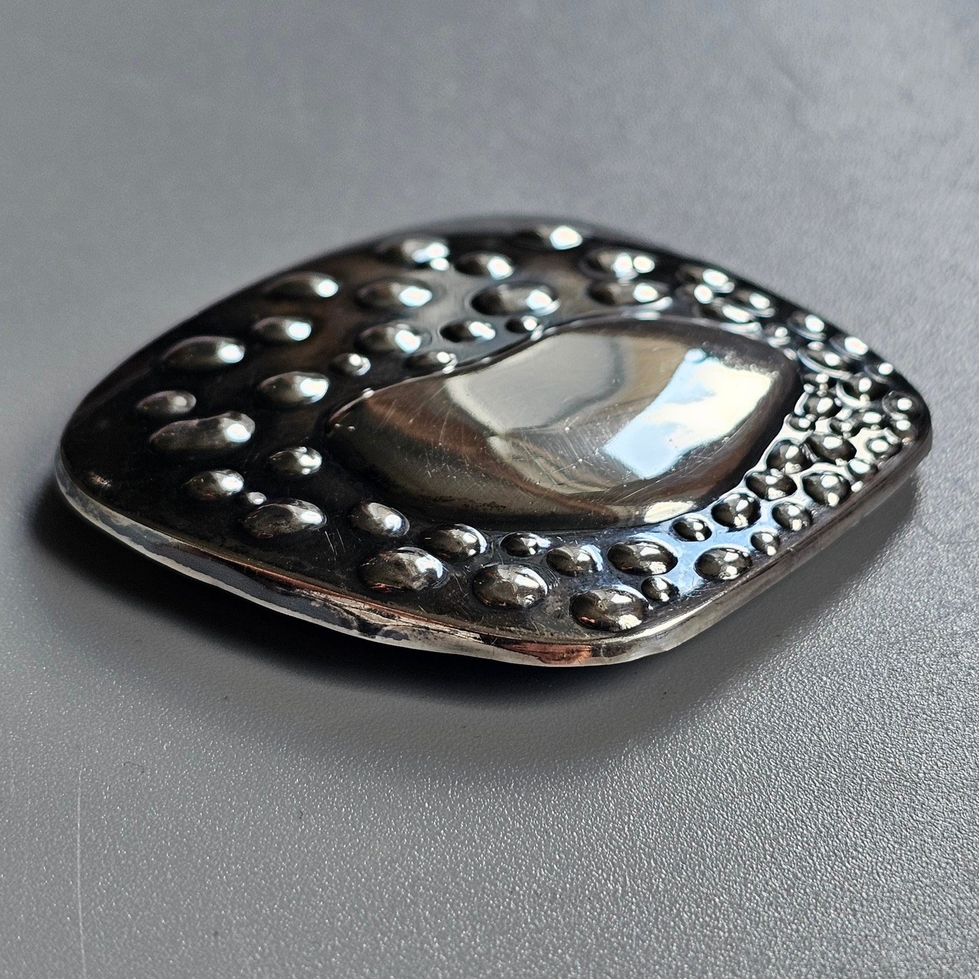 Decorative silver brooch or pendant with a polished center and textured border of raised dots.