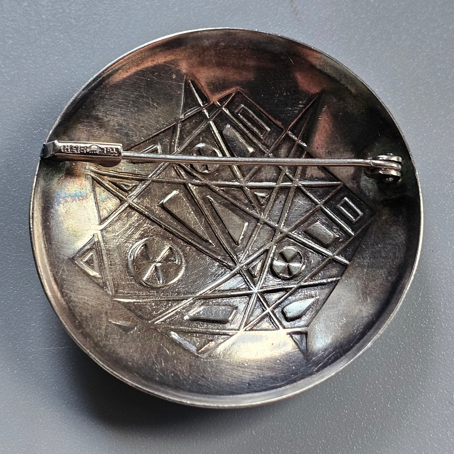 Metallic dish or plate with an engraved geometric pattern on its surface.