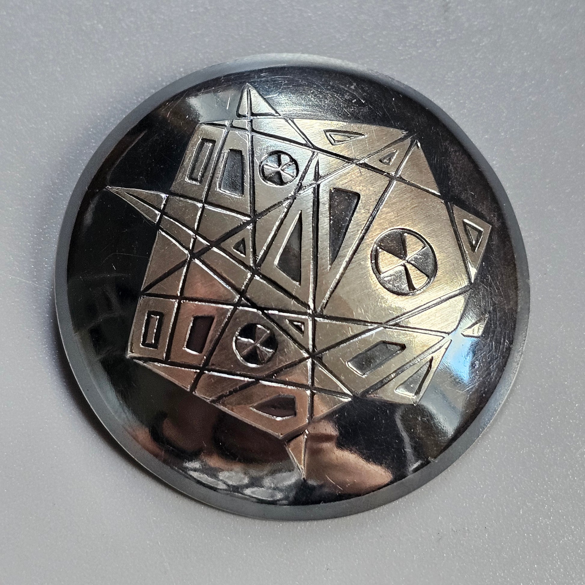 Metallic circular object with an engraved geometric pattern featuring stars and triangles.